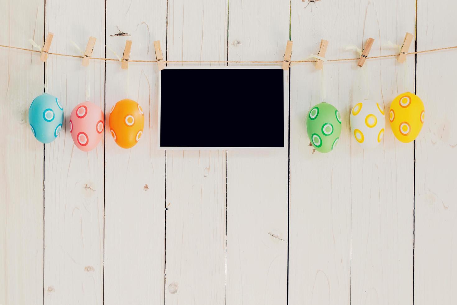 Easter egg and blank photo frame hanging on with white wood with space.