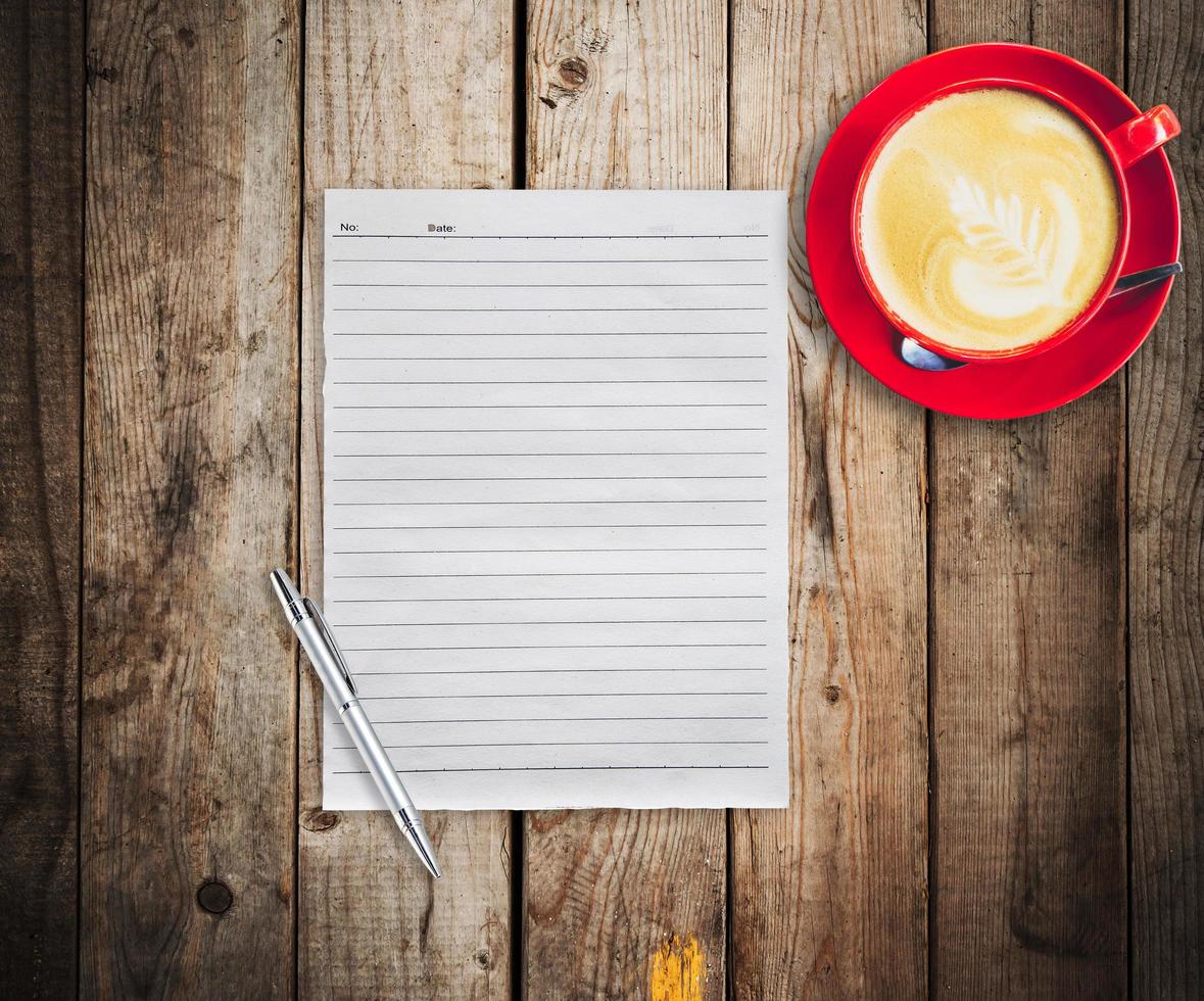 Empty paper and pen with red cup coffee on wood table background photo