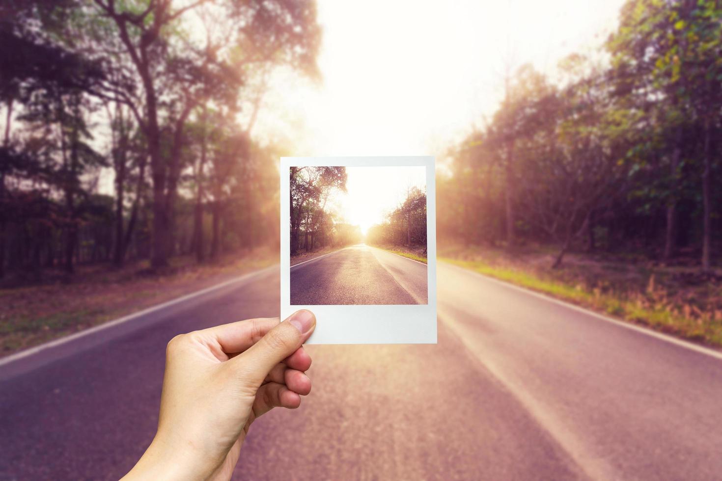 Hand holding photo frame empty asphalt road and sunset.