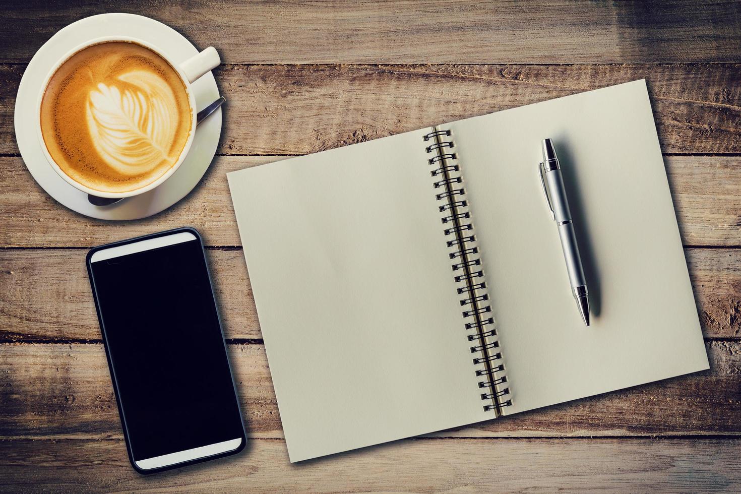 Top view notebook, pen, coffee cup, and phone on wood table, Vintage filter. photo