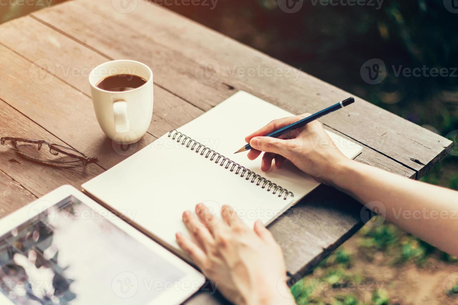 hembra mano con lápiz escritura en cuaderno. mujer mano con lápiz escritura en cuaderno a café tienda. foto