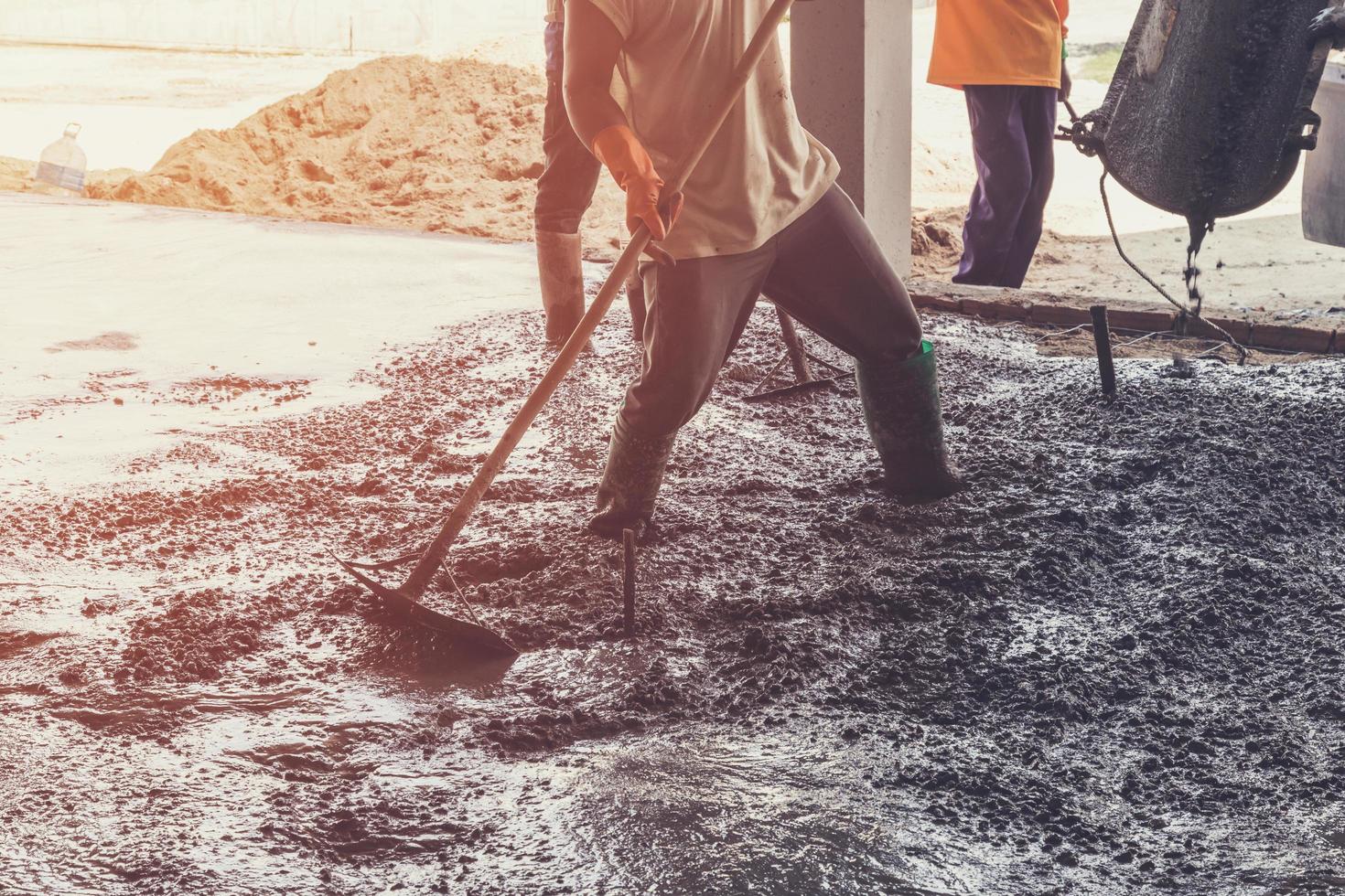 man workers spreading freshly poured concrete mix on building with vintage tone. photo