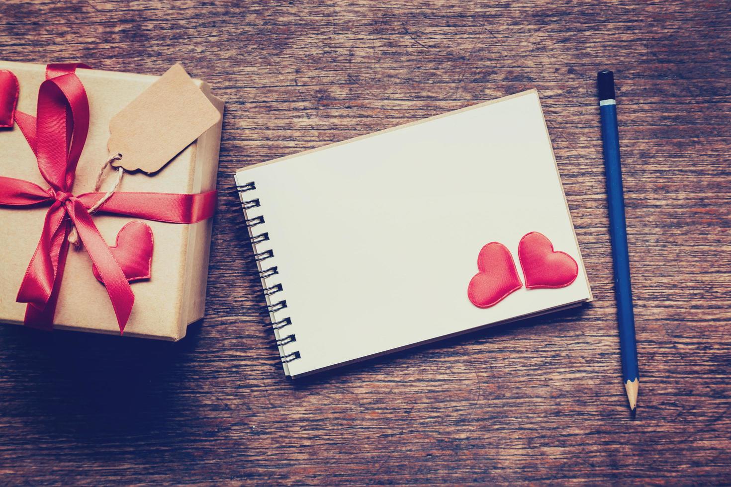 Top view gift box and red ribbon and red heart with notebook on table wooden. photo