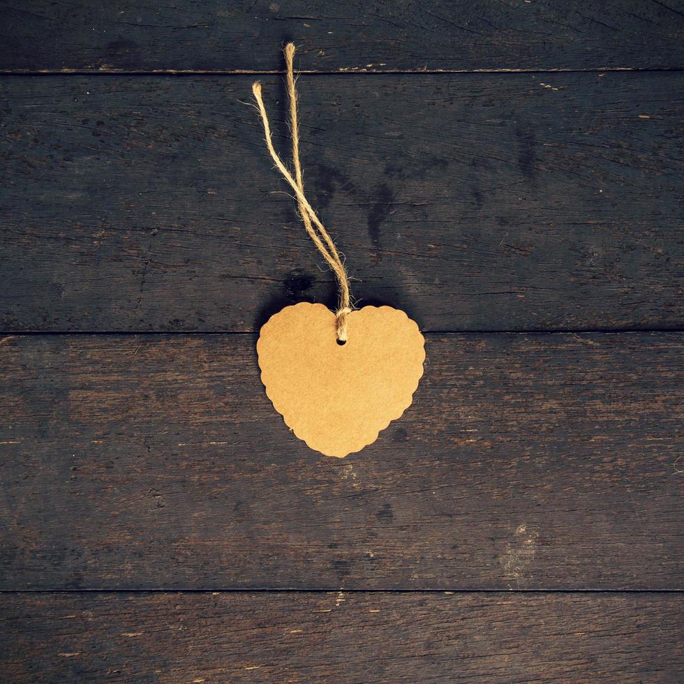 Blank brown tag heart shape on old wood background with space. photo