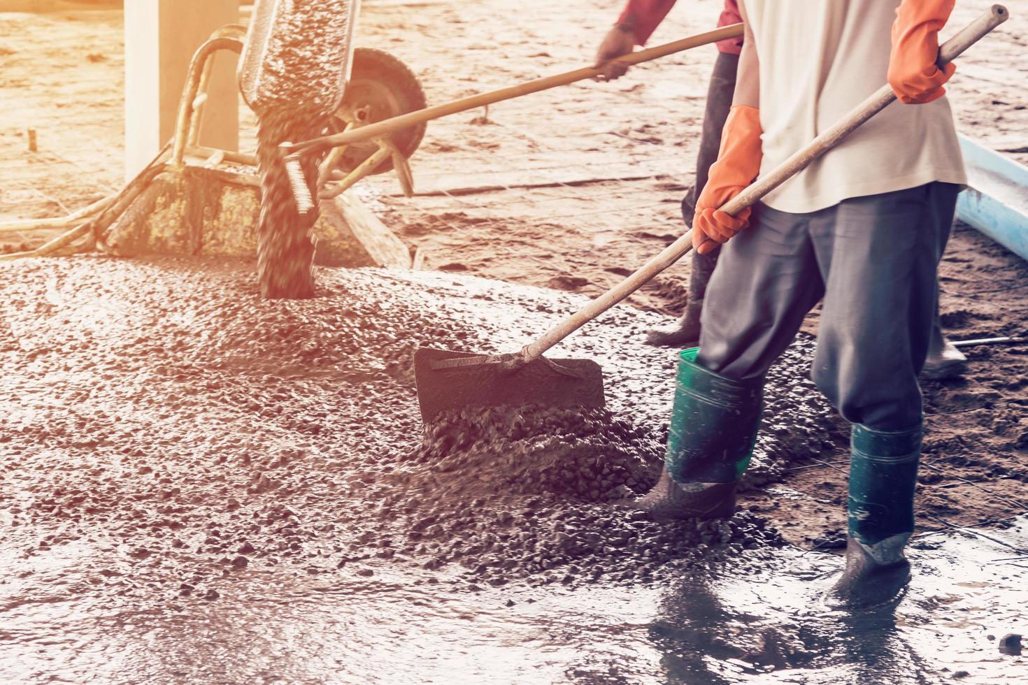 man workers spreading freshly poured concrete mix on building with vintage tone. photo