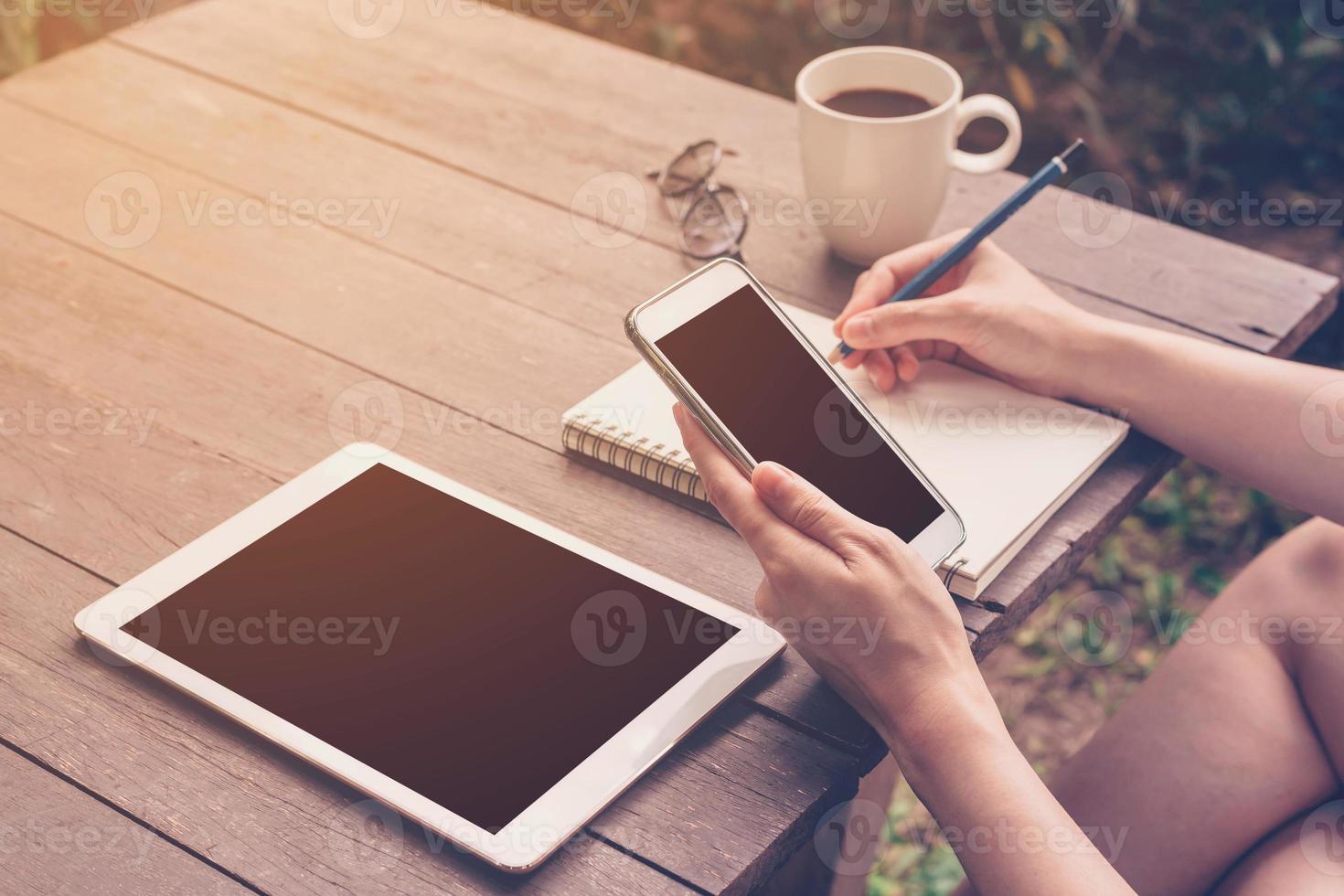 close up hand woman writing notebook and holding phone in coffee shop with vintage toned. photo