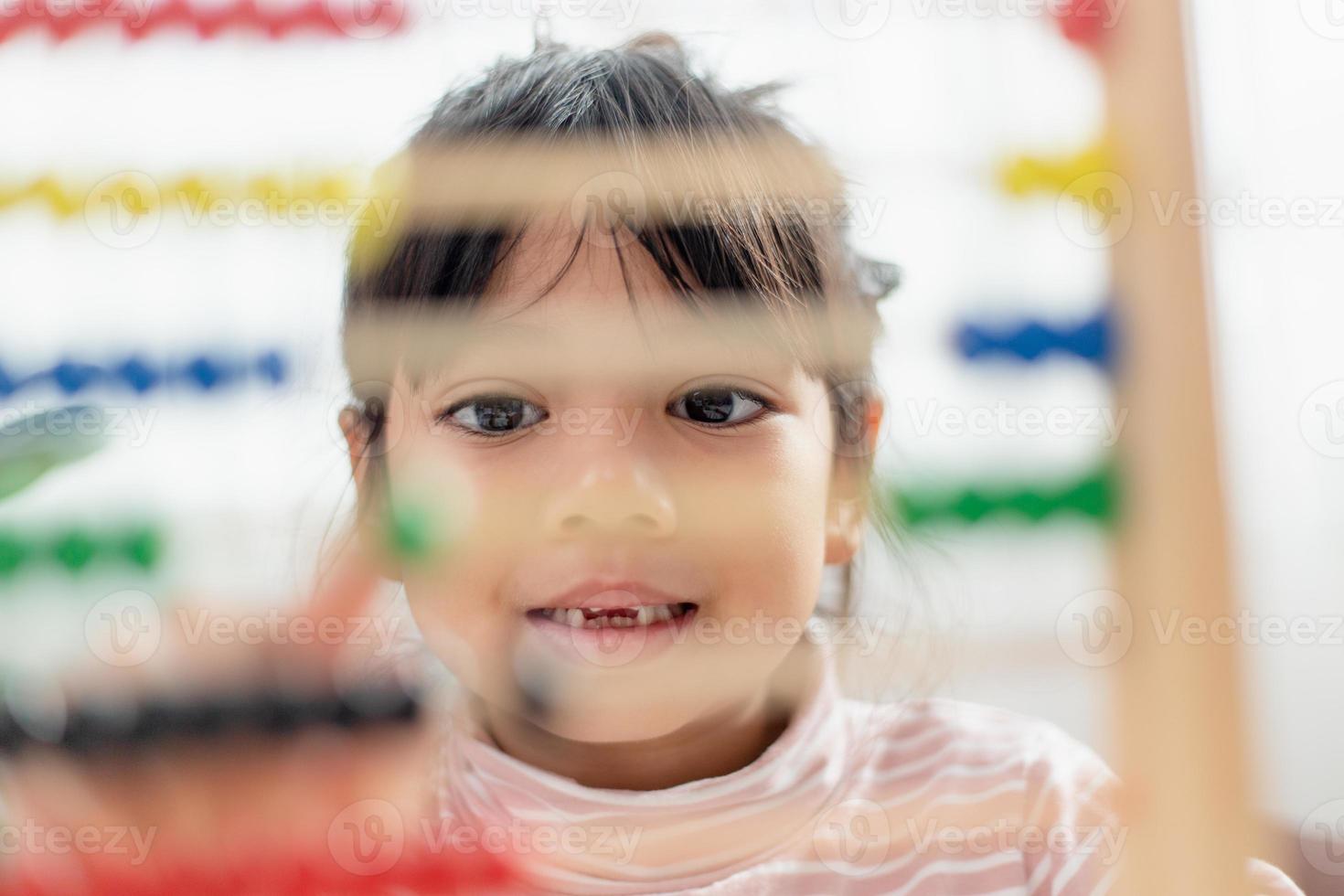 A young cute Asian girl is using the abacus with colored beads to learn how to count at home photo