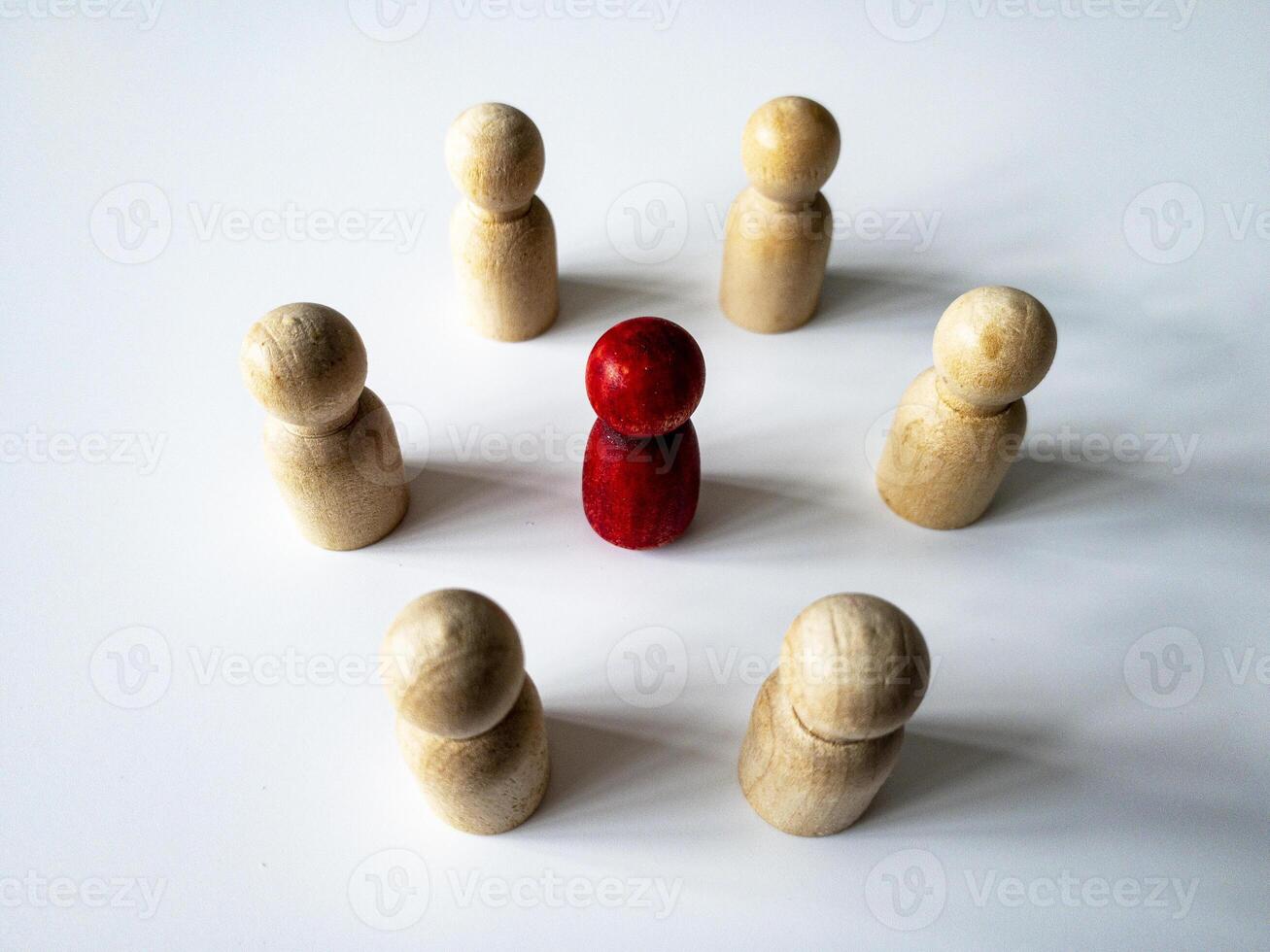 Top side view of red wooden doll figure surrounded by other doll figure. Harassment and bullying concept. photo