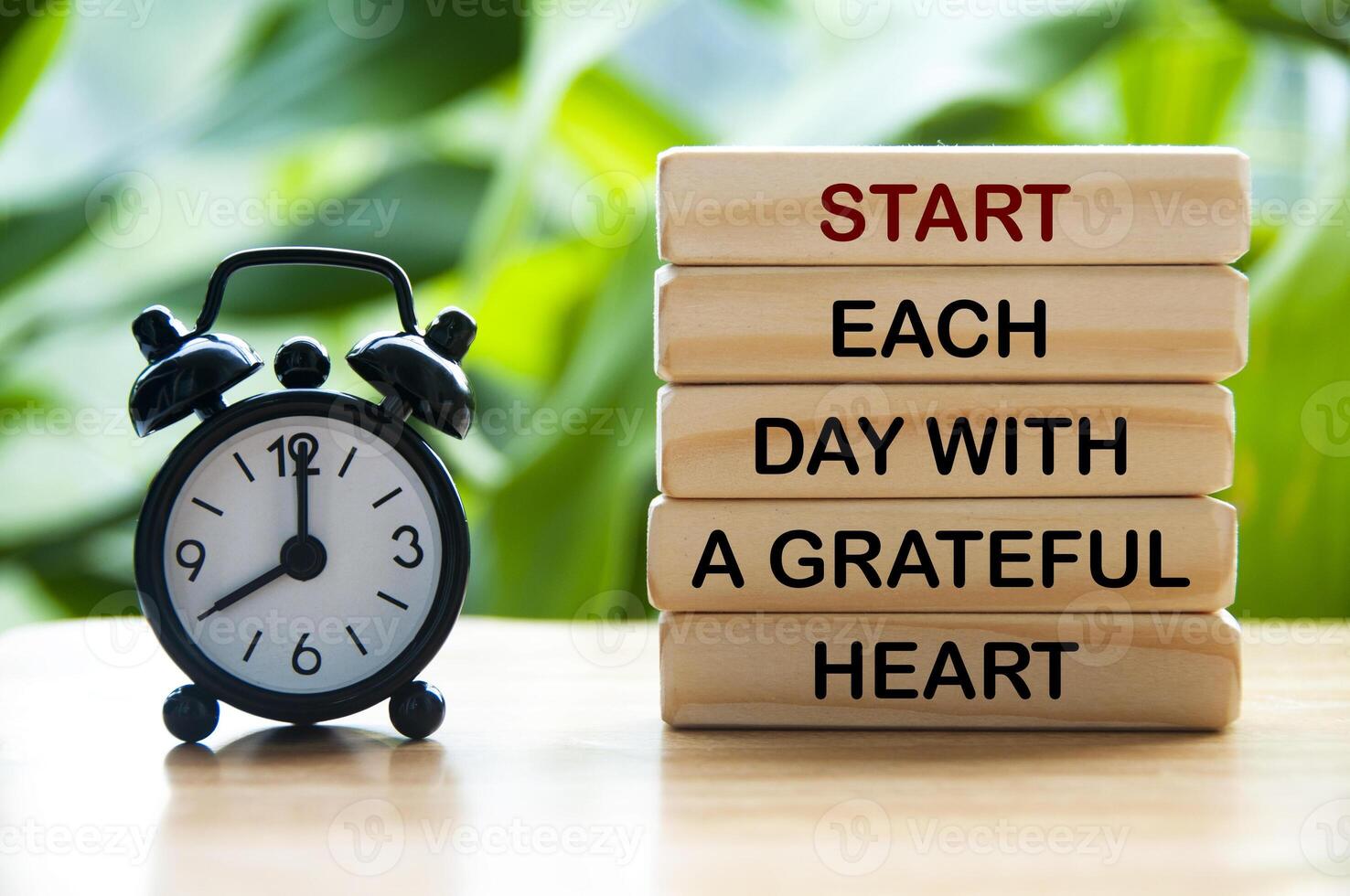 Start each day with a grateful heart text on wooden blocks with alarm clock and nature background. Motivational concept photo