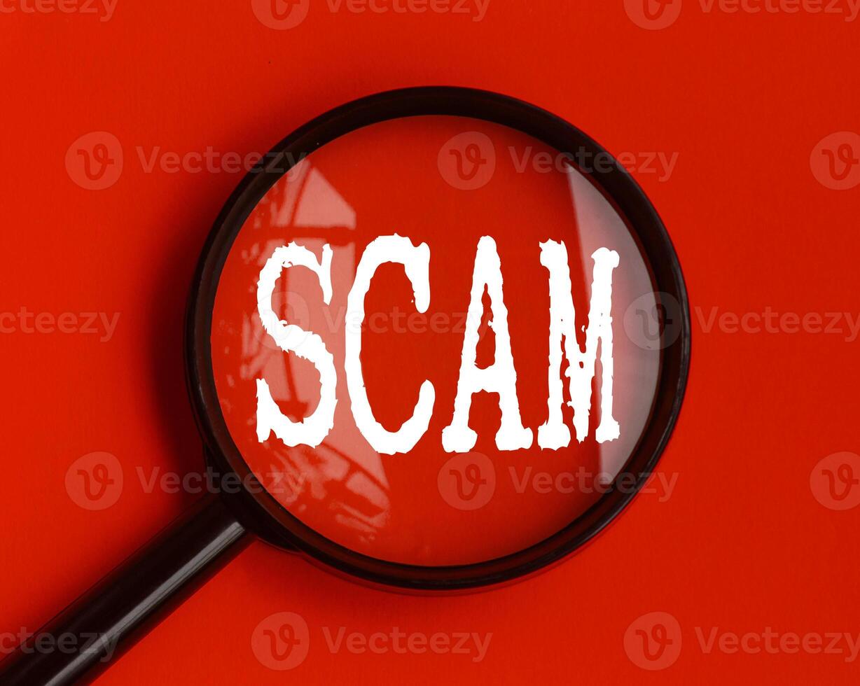 Scam text on red cover with magnifying glass. Scamming and fraud concept photo