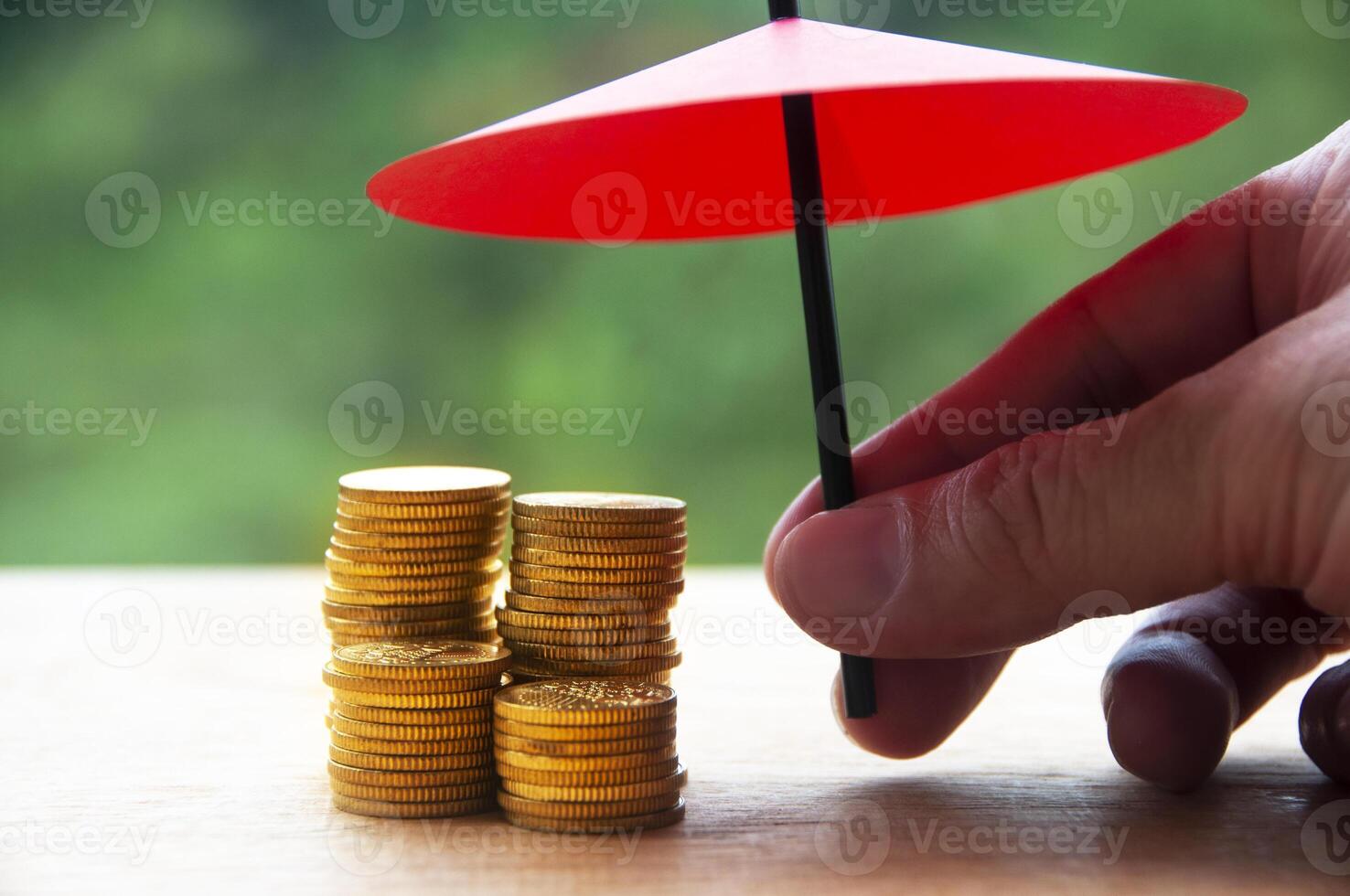 Umbrella covering gold coin with blurred nature background. Security, financial independence, assurance and safety concept photo