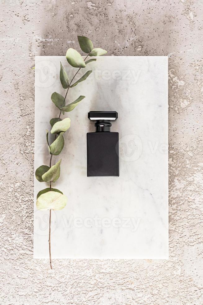 Vertical view of an elegant black matte bottle of men's cosmetic or spray on a rectangular slice of marble. gray concrete background. nameless bottle. photo