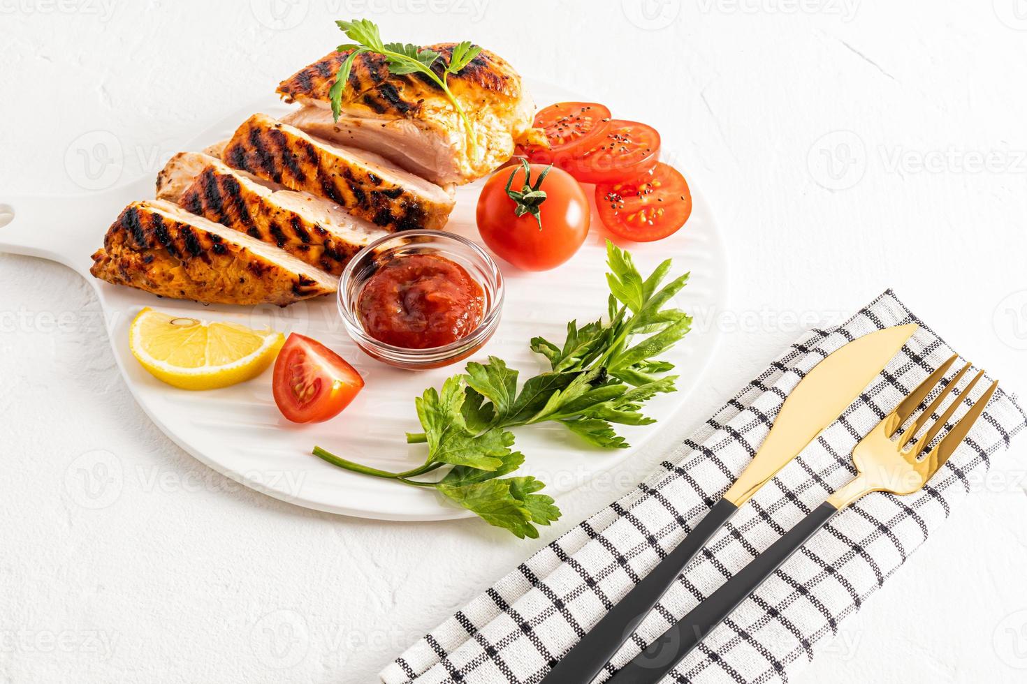 A freshly prepared piece of grilled chicken breast fillet is served on a serving dish with fresh vegetables and lemon slices. white background. menu. photo