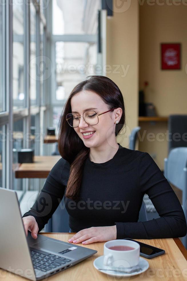 Beautiful businesswoman working on laptop in coffee shop. Female freelancer connecting to internet via computer. Blogger or journalist writing new article. photo