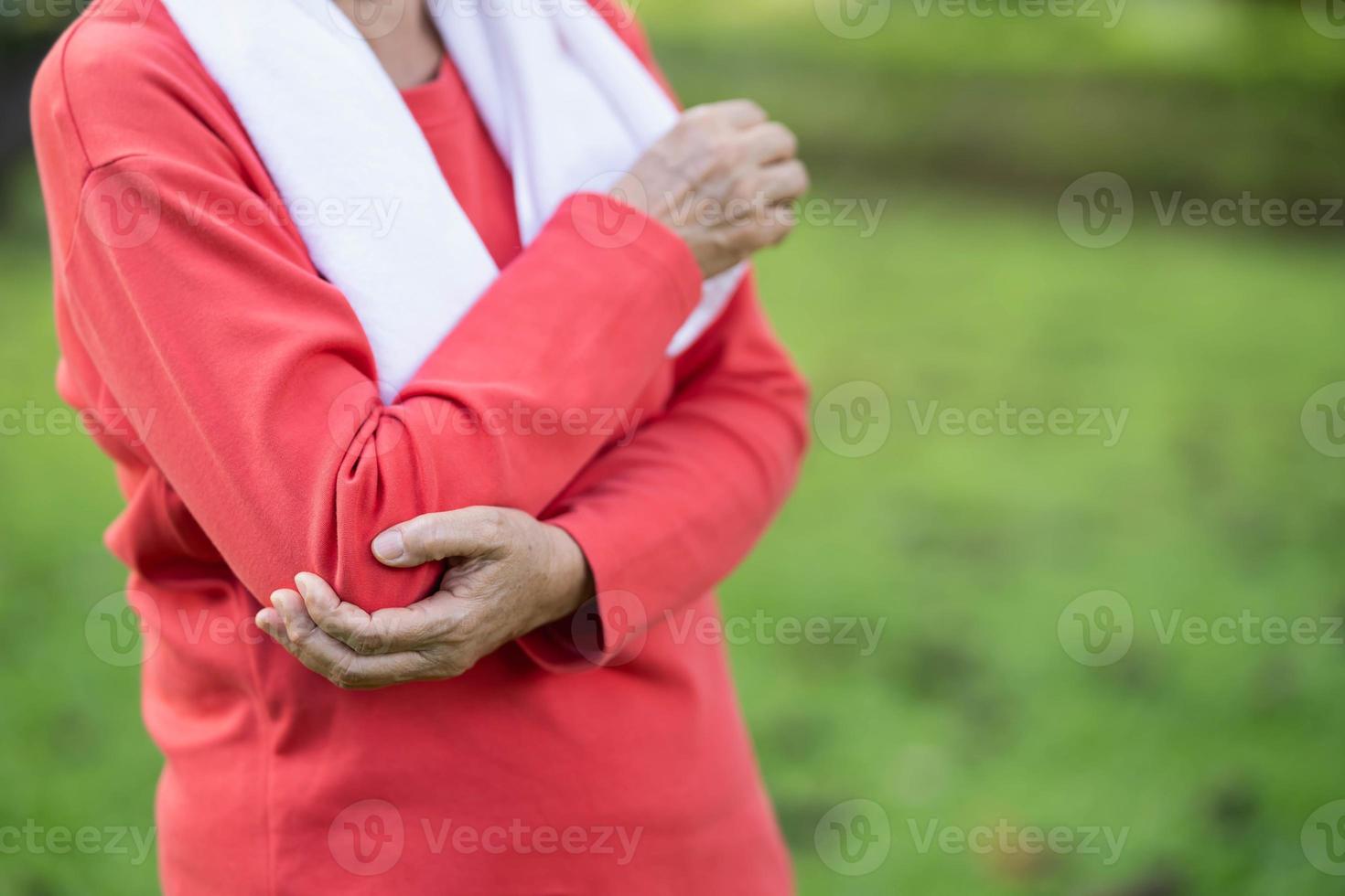 Senior asian woman hold arm or elbow pain after running in park. Old asian woman resting at the park garden and holding painful elbow. Sport and health concept. photo