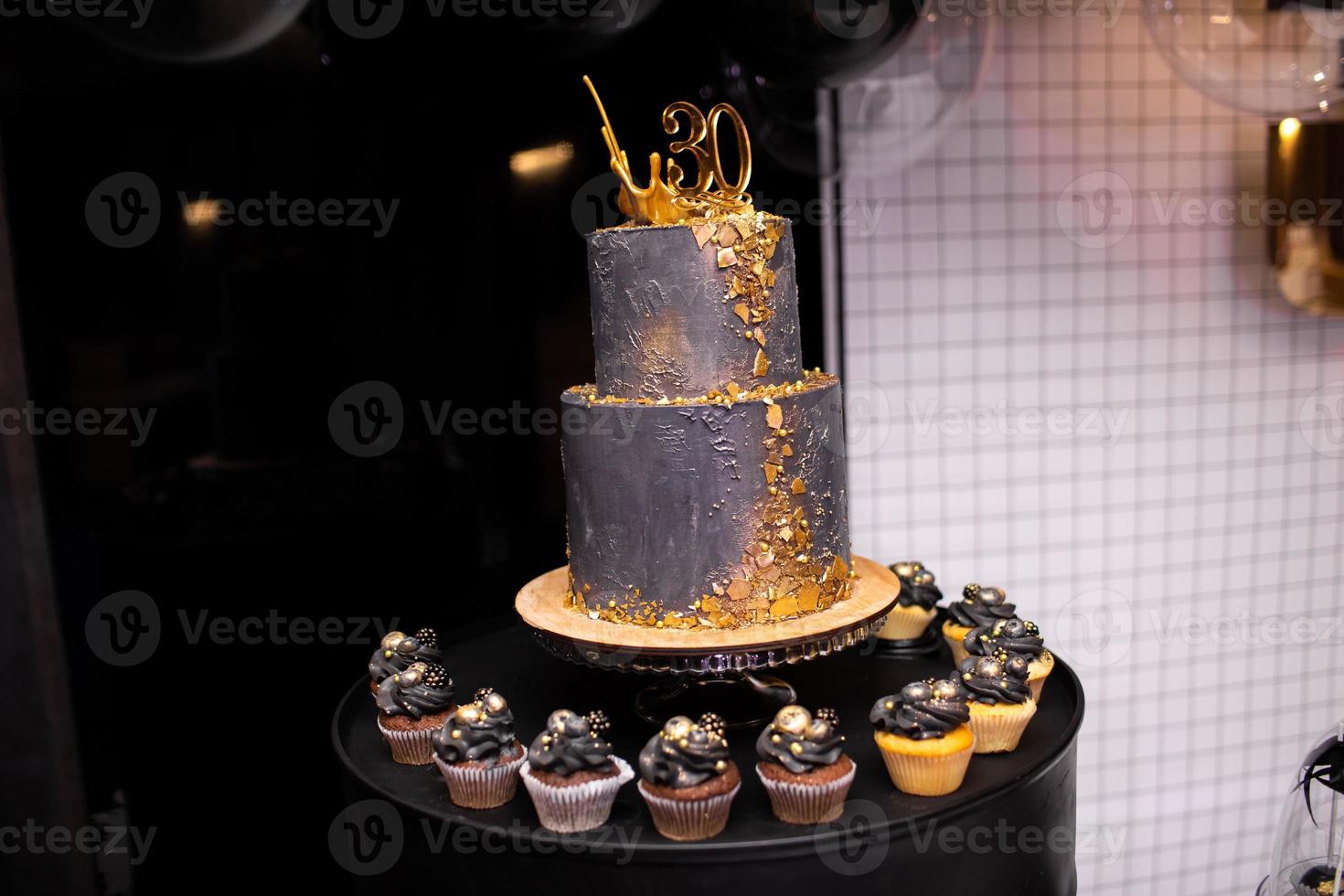 festivo dos niveles negro pastel con oro decoración para el 30 aniversario. muchos chocolate y vainilla magdalenas con lujo decoración. barra de caramelo para cumpleaños foto