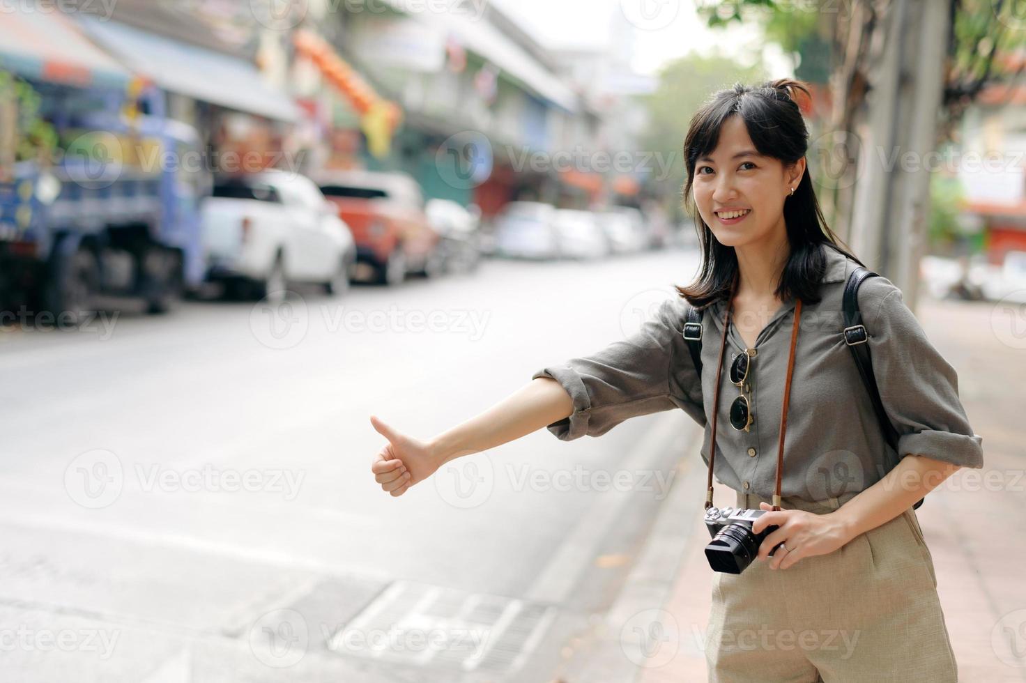 Smiling young Asian woman traveler hitchhiking on a road in the city. Life is a journey concept. photo