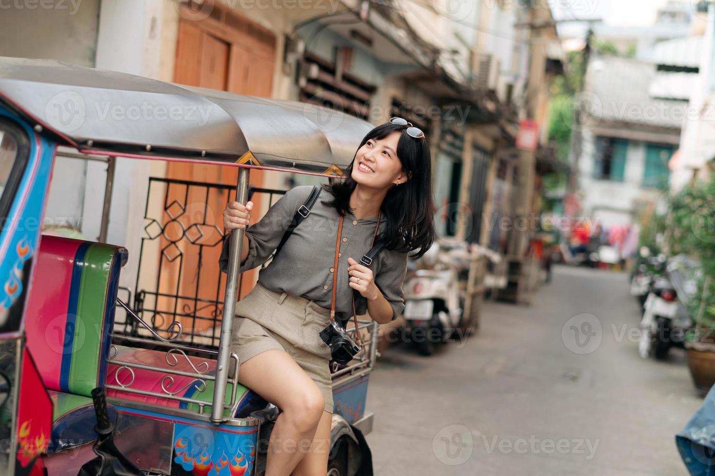 Young Asian woman backpack traveler standing a side of Tuk Tuk taxi on summer vacations at Bangkok, Thailand. photo