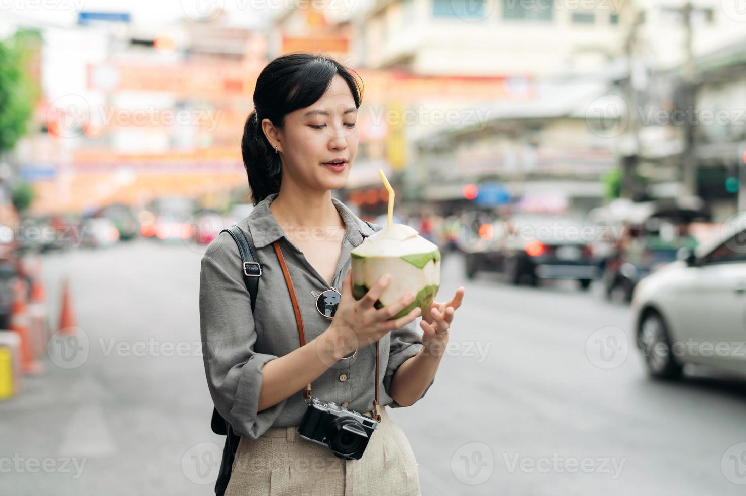 Happy young Asian woman backpack traveler drinking a coconut juice at China town street food market in Bangkok, Thailand. Traveler checking out side streets. photo