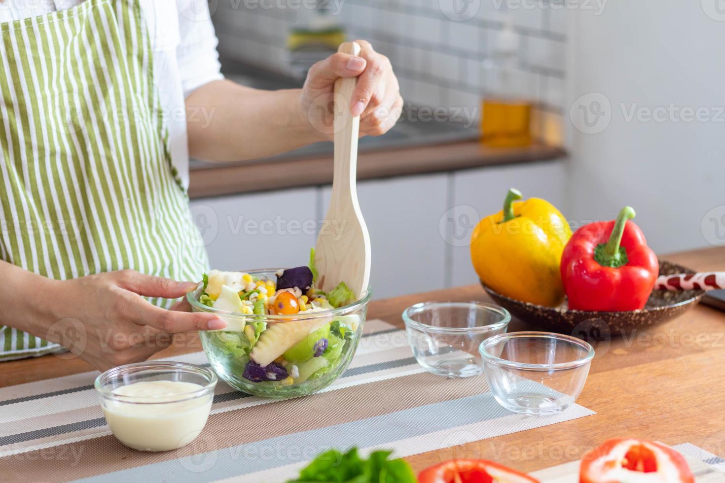 young woman is making salad from vegetables she has prepared on table in her home kitchen to get salad that is clean and safe because ingredients are carefully selected. healthy food preparation ideas photo