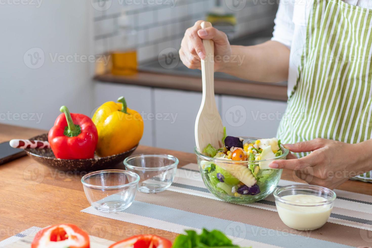 young woman is making salad from vegetables she has prepared on table in her home kitchen to get salad that is clean and safe because ingredients are carefully selected. healthy food preparation ideas photo