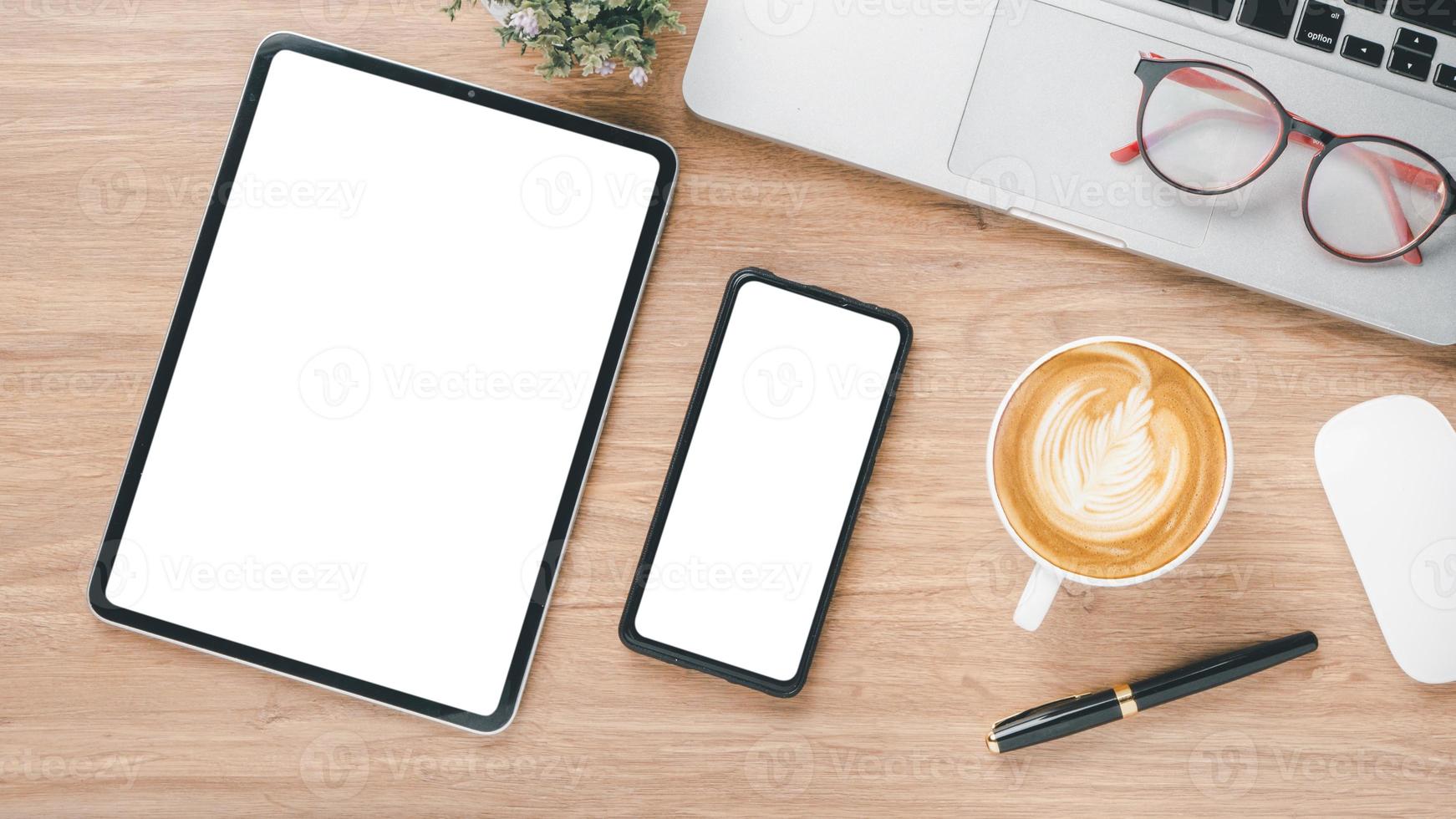 Wooden desk workplace with blank screen digital tablet and smartphone, laptop, eyeglass, mouse, pen and cup of coffee, Top view flat lay. photo