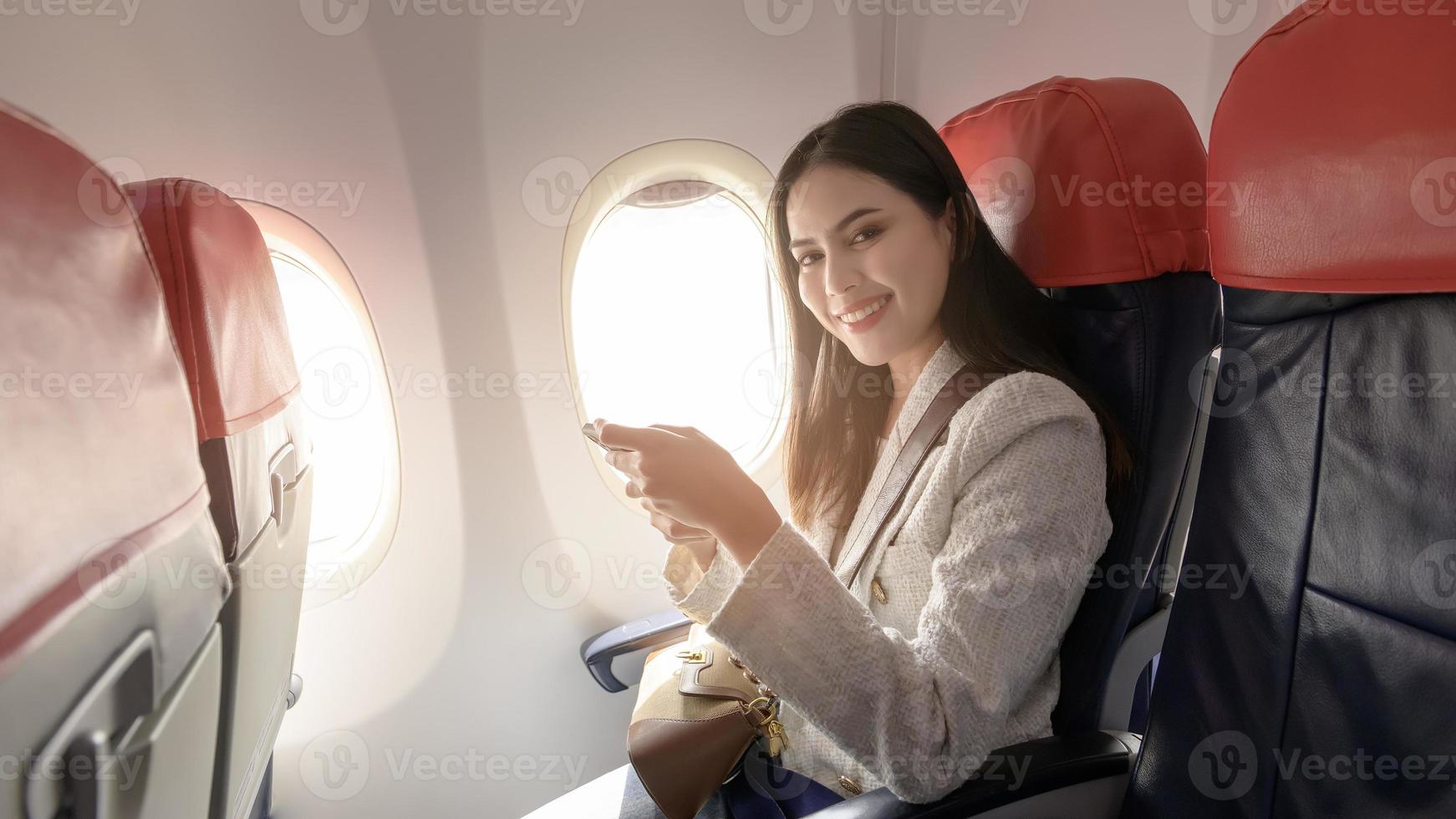 hermosa asiático mujer es trabajando con teléfono inteligente y tableta en avión foto