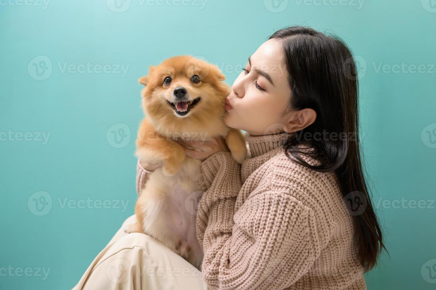 Portrait of Young beautiful woman kisses and hugs her dog over green background. photo