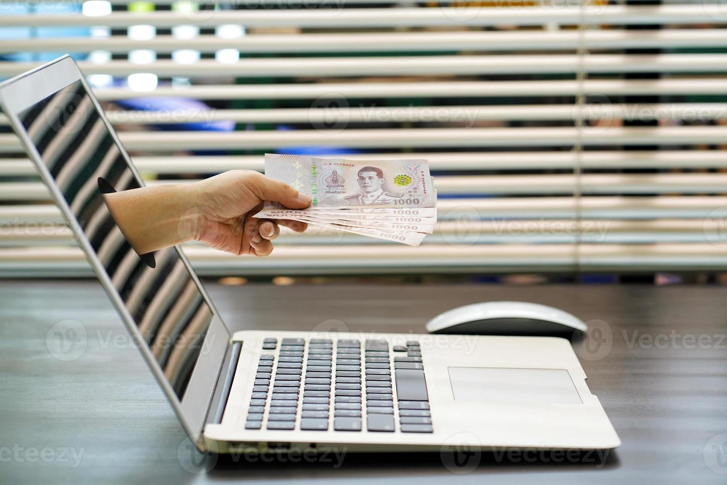 Hand holding Thai 5000 baht banknotes coming out from computer screen.concept Registration for 5,000 baht government aid, for people affected by the  covid19 or coronavirus crisis photo