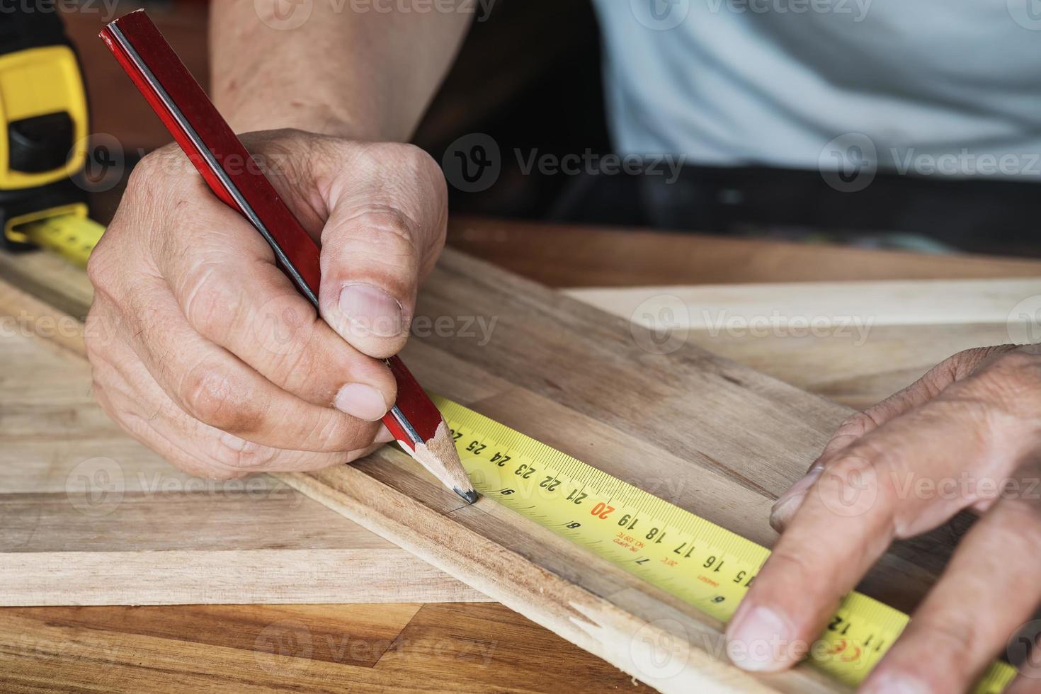 Carpenter using a measuring tape and mark a cut line with pencil on a wood board.DIY maker and woodworking concept. selective focus photo