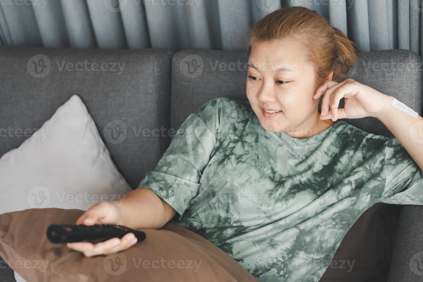 el ama de casa asiática se sienta en el sofá y sostiene el control remoto viendo la televisión con una acción relajante. concepto de estilo de vida de hobby y tiempo libre. foto