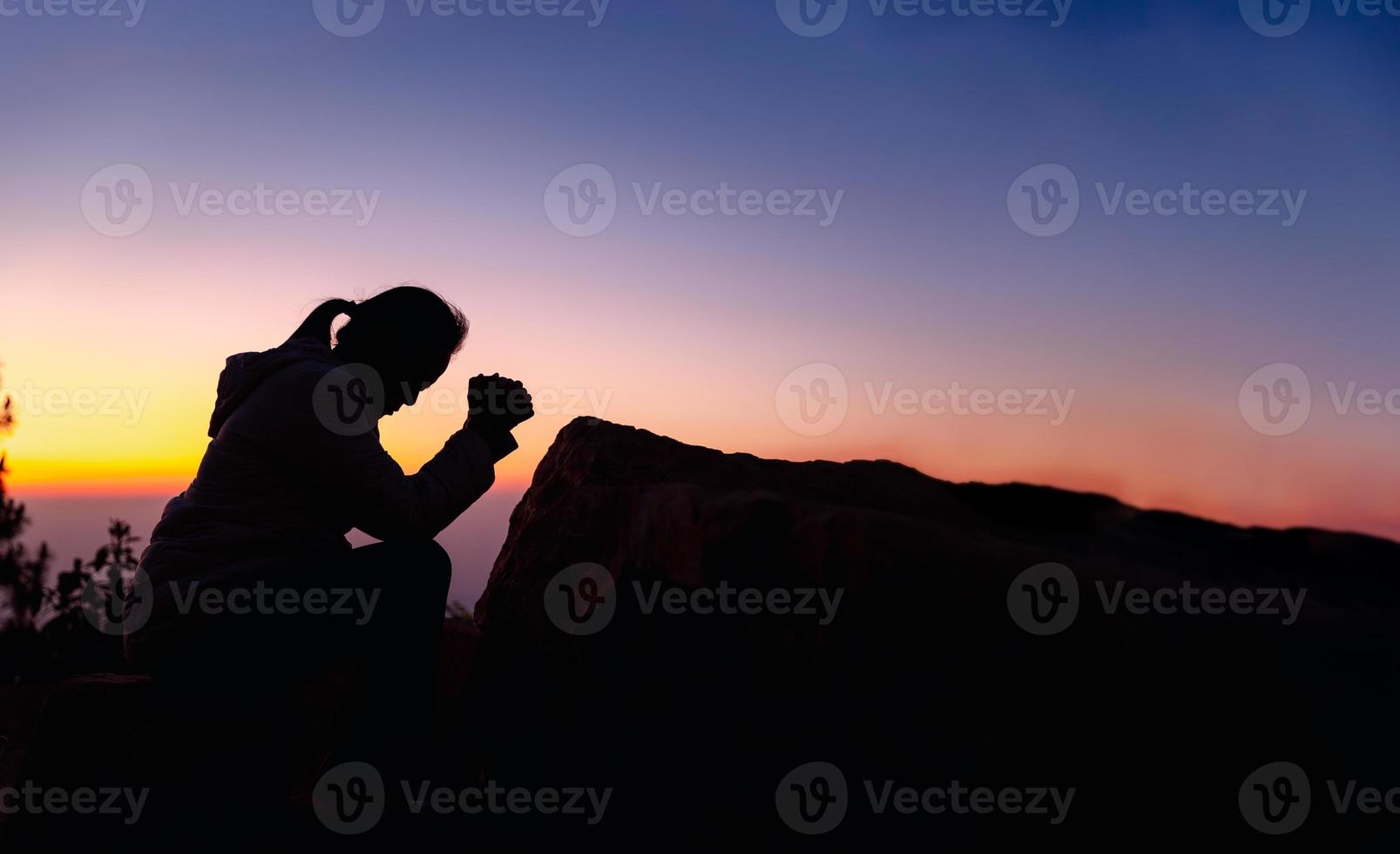 Silhouette of woman kneeling down praying for worship God at sky background. Christians pray to jesus christ for calmness. In morning people got to a quiet place and prayed. Banner with copy space. photo