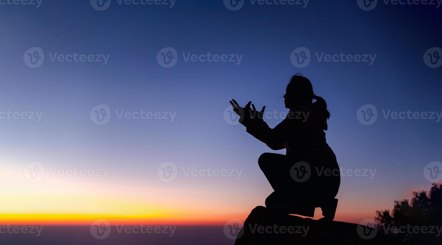 Silhouette of woman kneeling down praying for worship God at sky background. Christians pray to jesus christ for calmness. In morning people got to a quiet place and prayed. Banner with copy space. photo