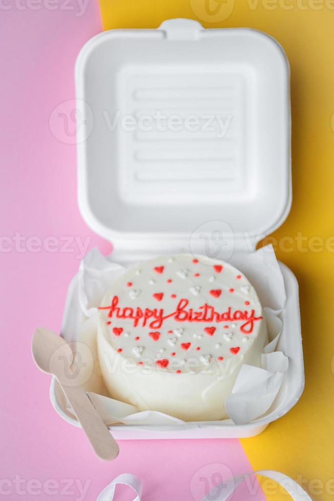 A small bento birthday cake in a box with a wooden spoon. Yellow and pink background photo