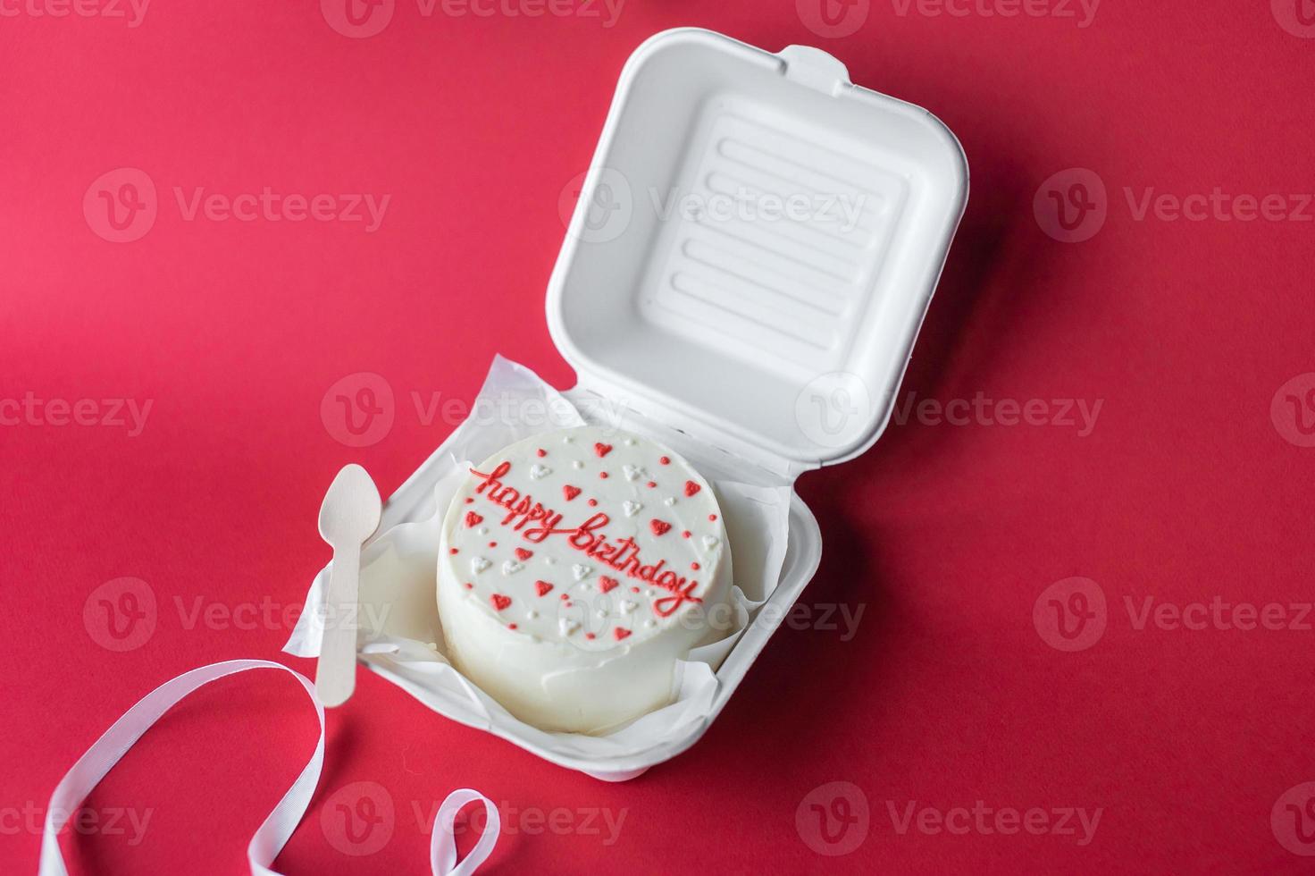 A small bento cake with lettering and hearts in a box with a wooden spoon. Red background photo