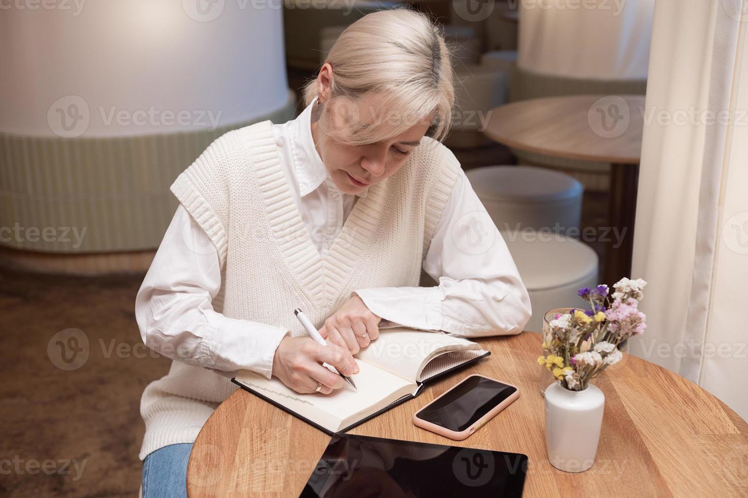 A cute girl is sitting in a cafe and making notes in a diary photo