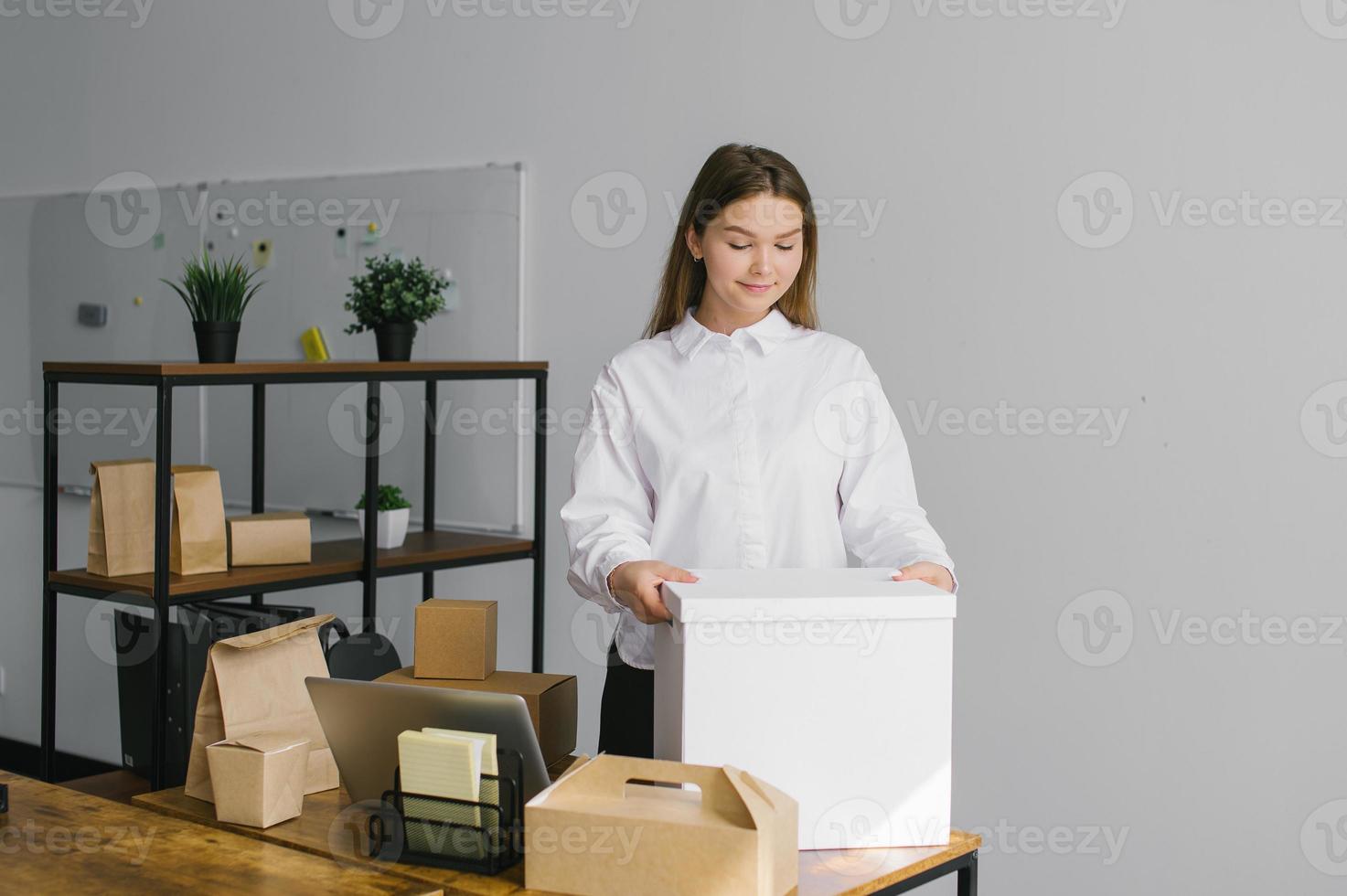 un linda niña es en pie en el oficina con un grande blanco papel caja foto