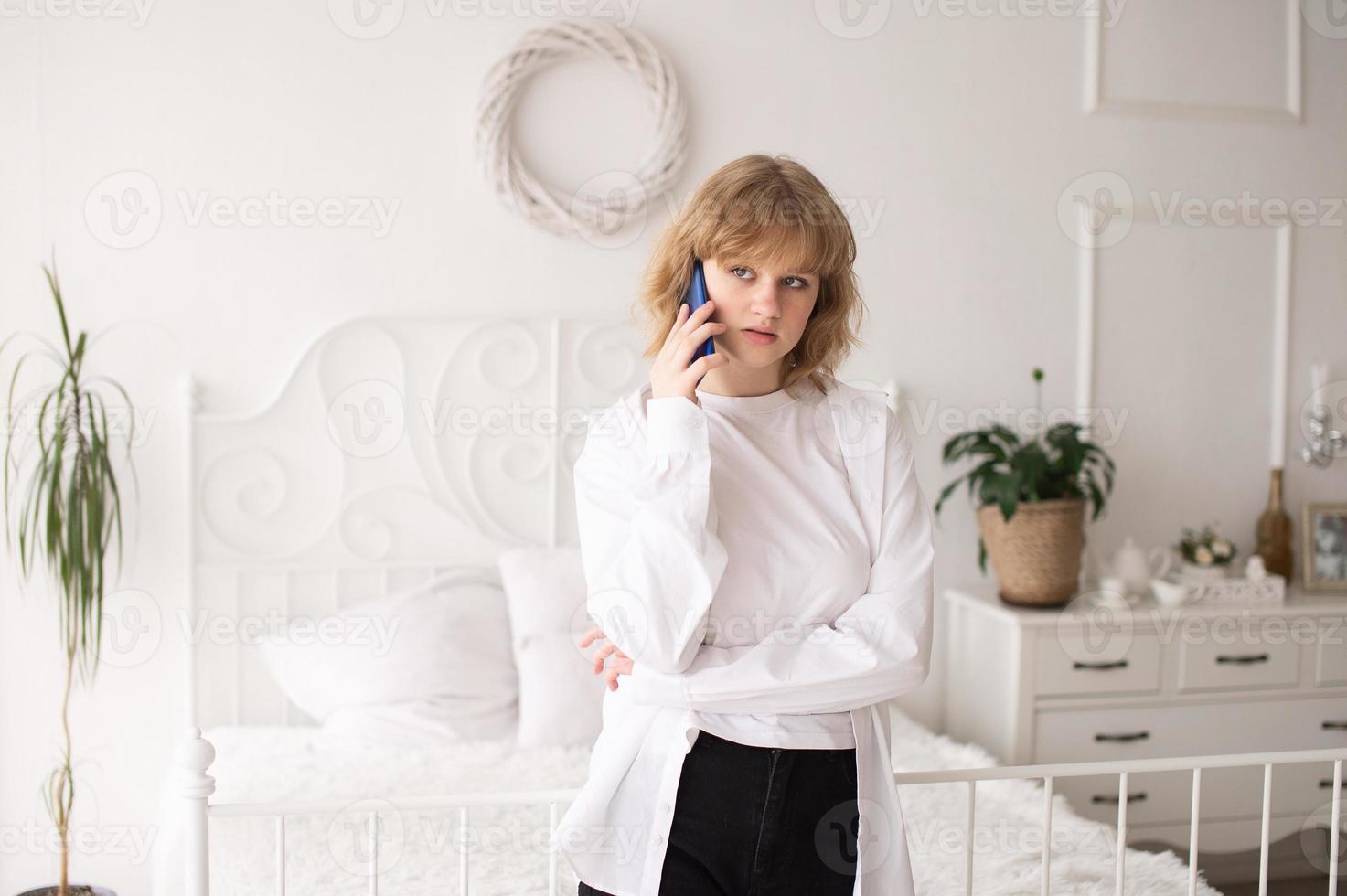 un educado en casa alumno. en pie con un teléfono en un blanco habitación foto