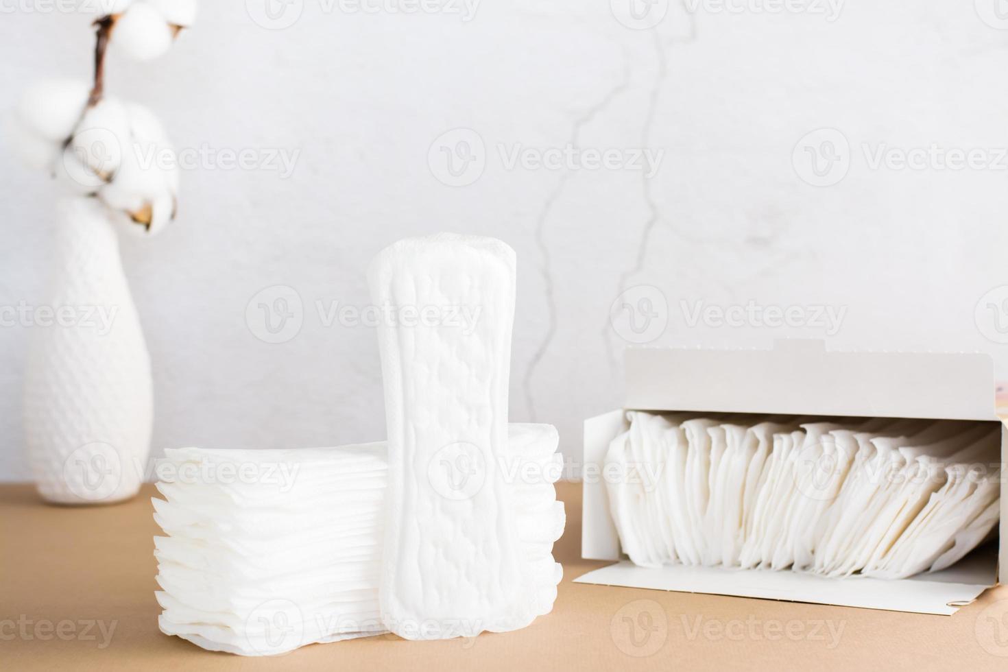 Clean disposable sanitary pads in a stack and in a box and a branch of cotton on a beige background. Women's health and comfort concept. Copy space photo