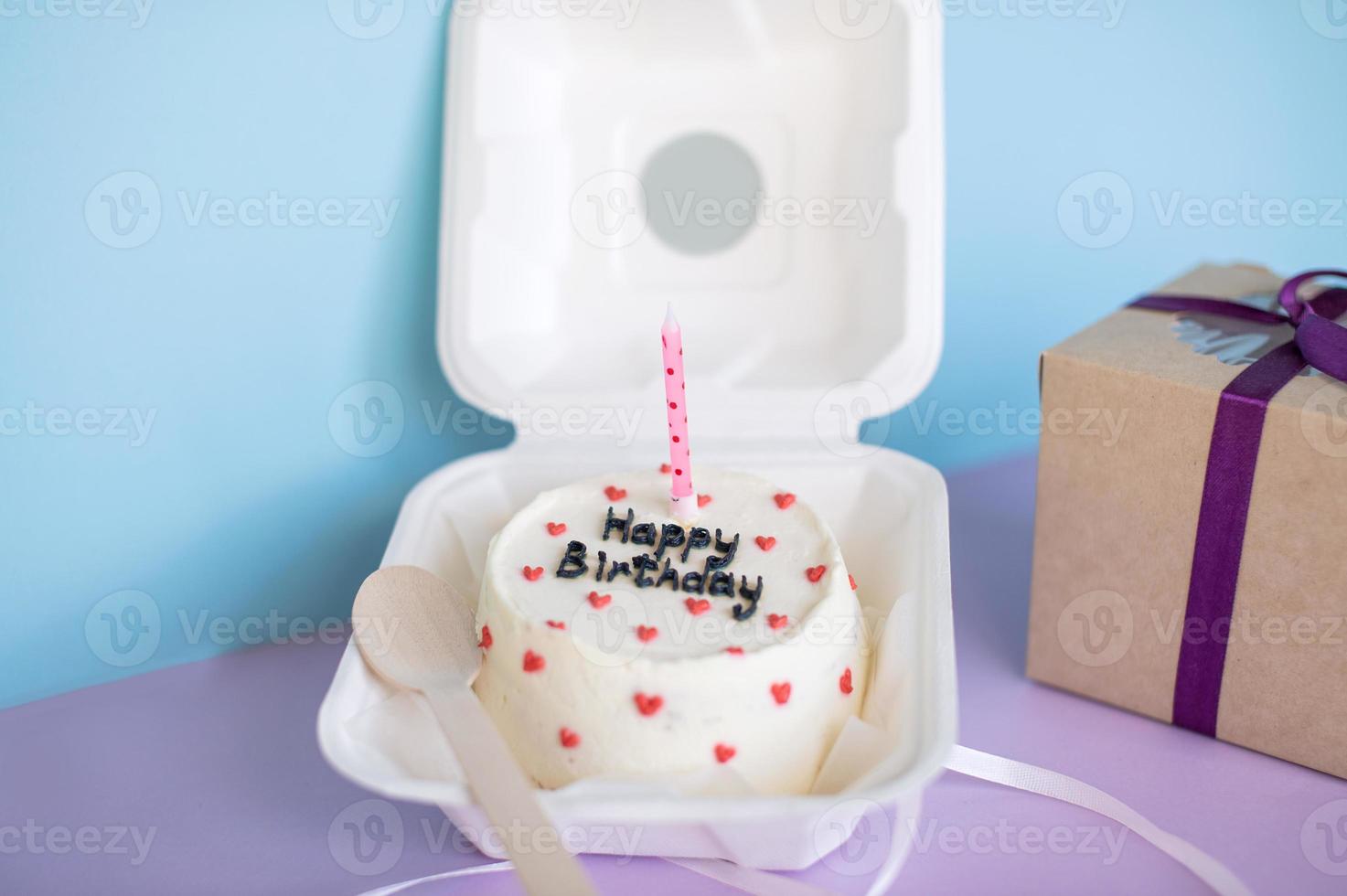 Birthday cake Bento in eco-packaging with a wooden spoon with a candle next to a gift on a purple-blue background photo
