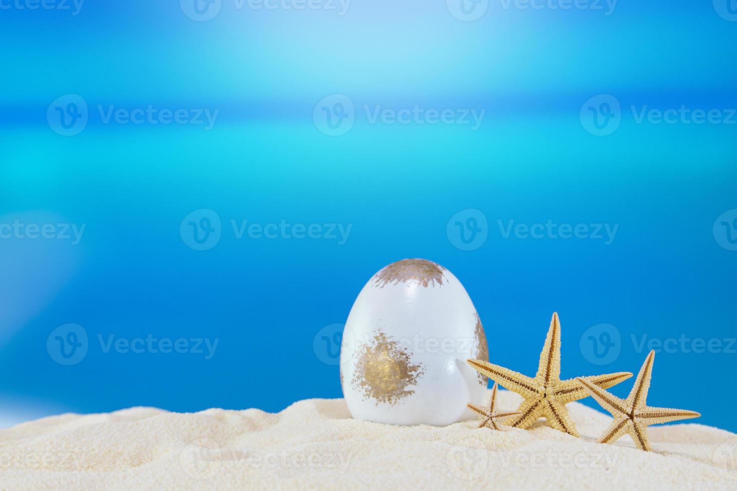 White gold egg with starfish on sandy beach of sea or ocean. Holiday postcard in sunny country. Happy easter. Travel, spring, summer. Copy space photo