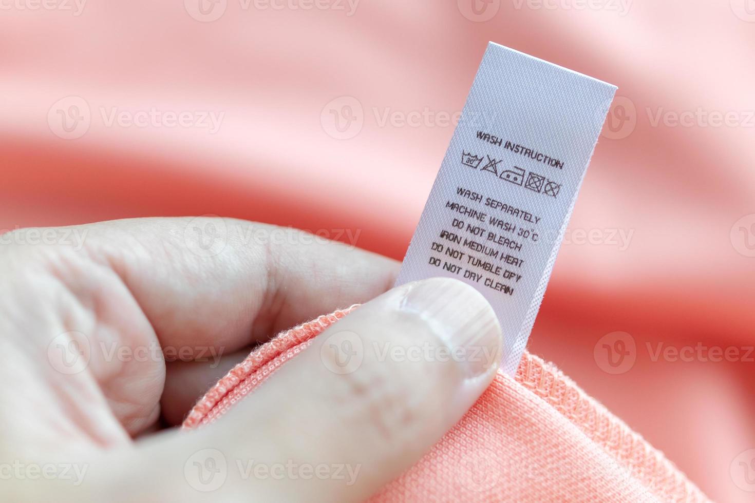 Hand hold and reading at white laundry care washing instructions clothes label on pink shirt photo