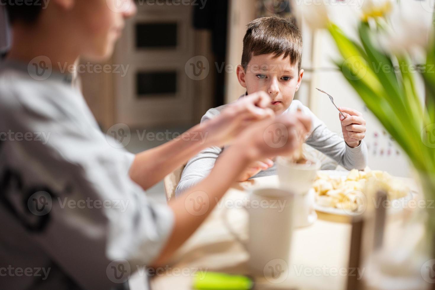 niños comer frutas y postres, bebida té a hogar en el noche cocina. chocolate en un palo para derritiendo. foto