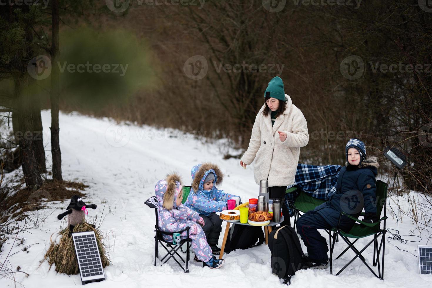 Young woman with children in winter forest on a picnic. Mother and three kids. photo