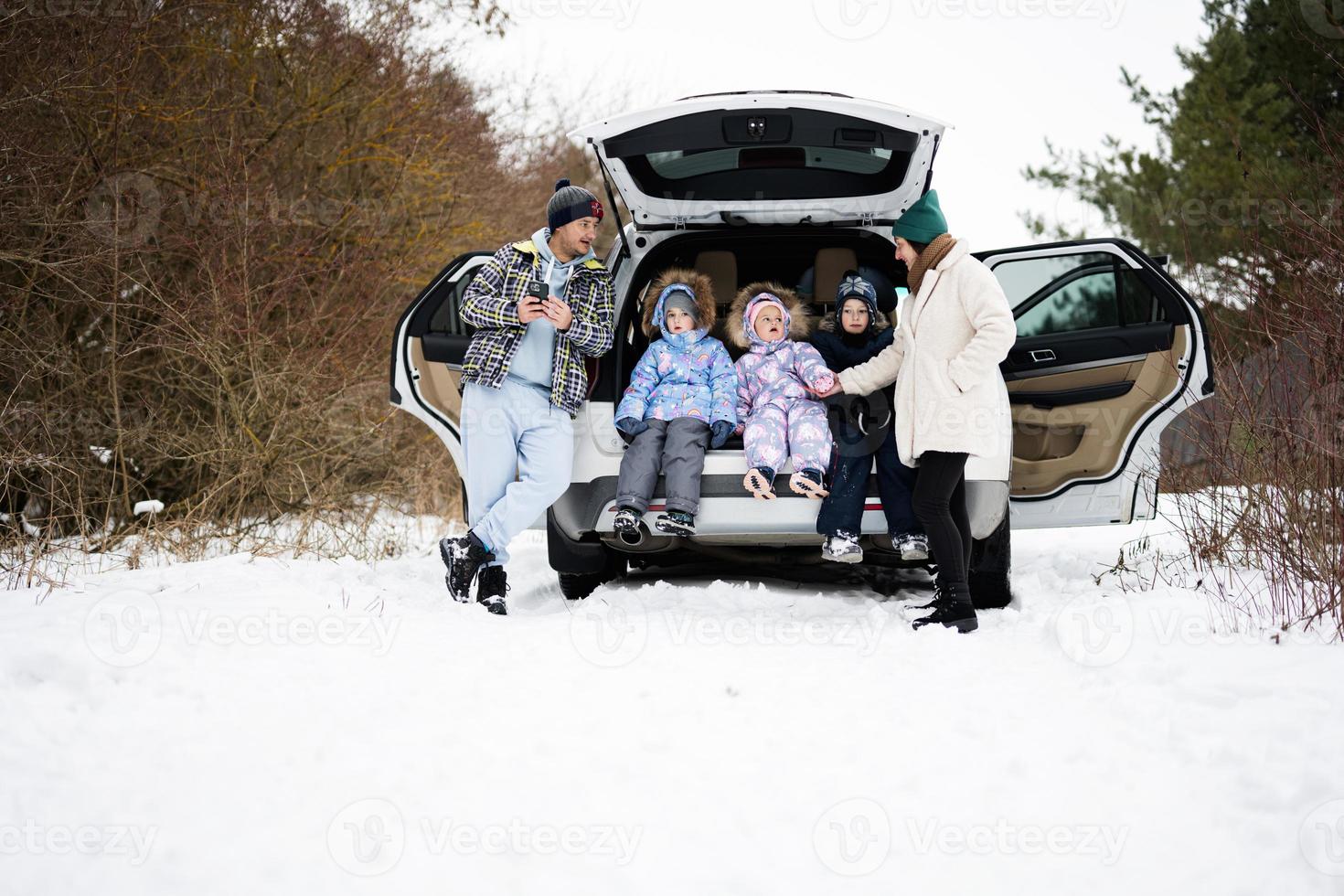 Family with kids sit on car suv with open trunk stand in winter forest. photo