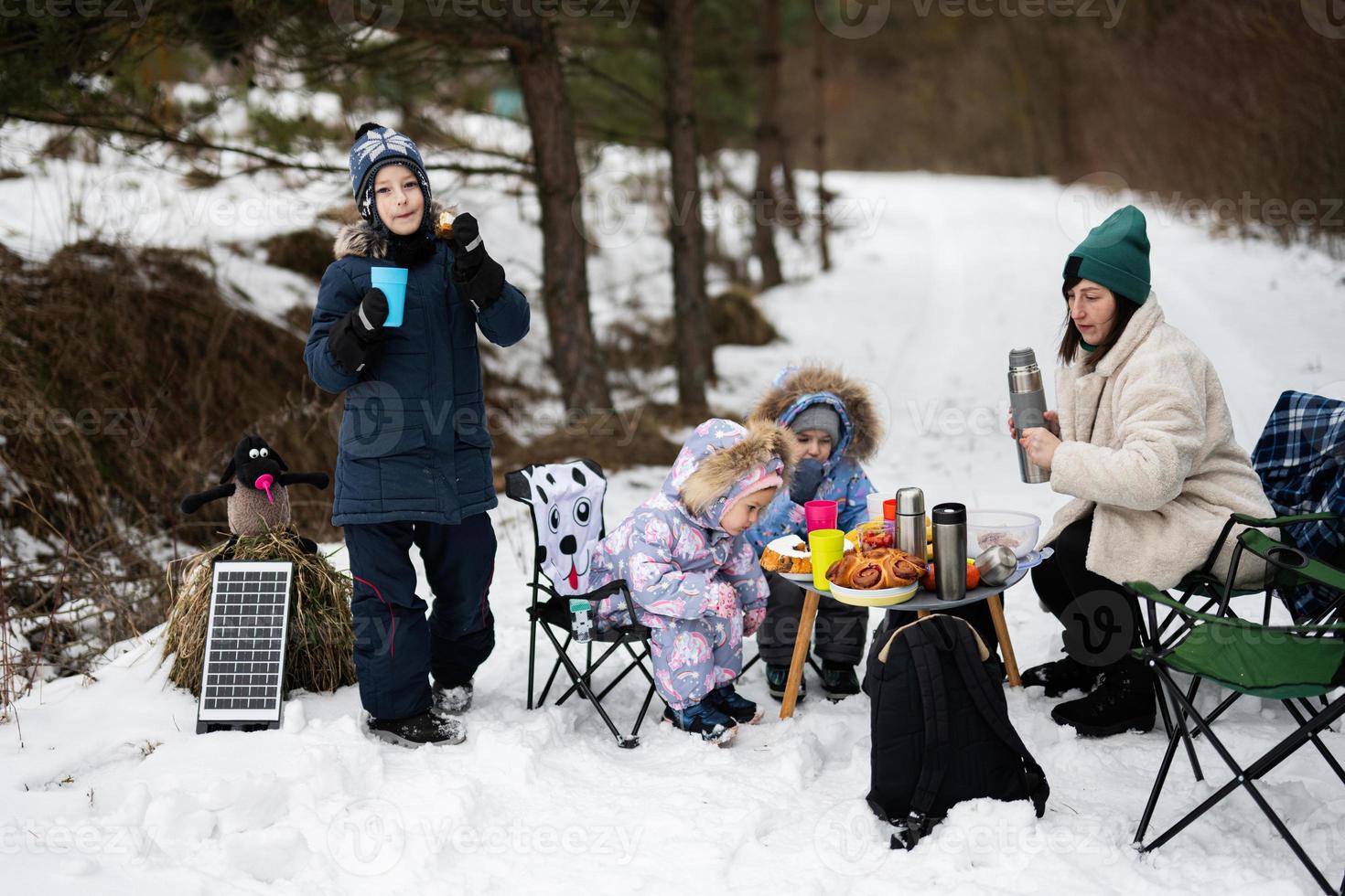 Young woman with children in winter forest on a picnic. Mother and three kids. photo