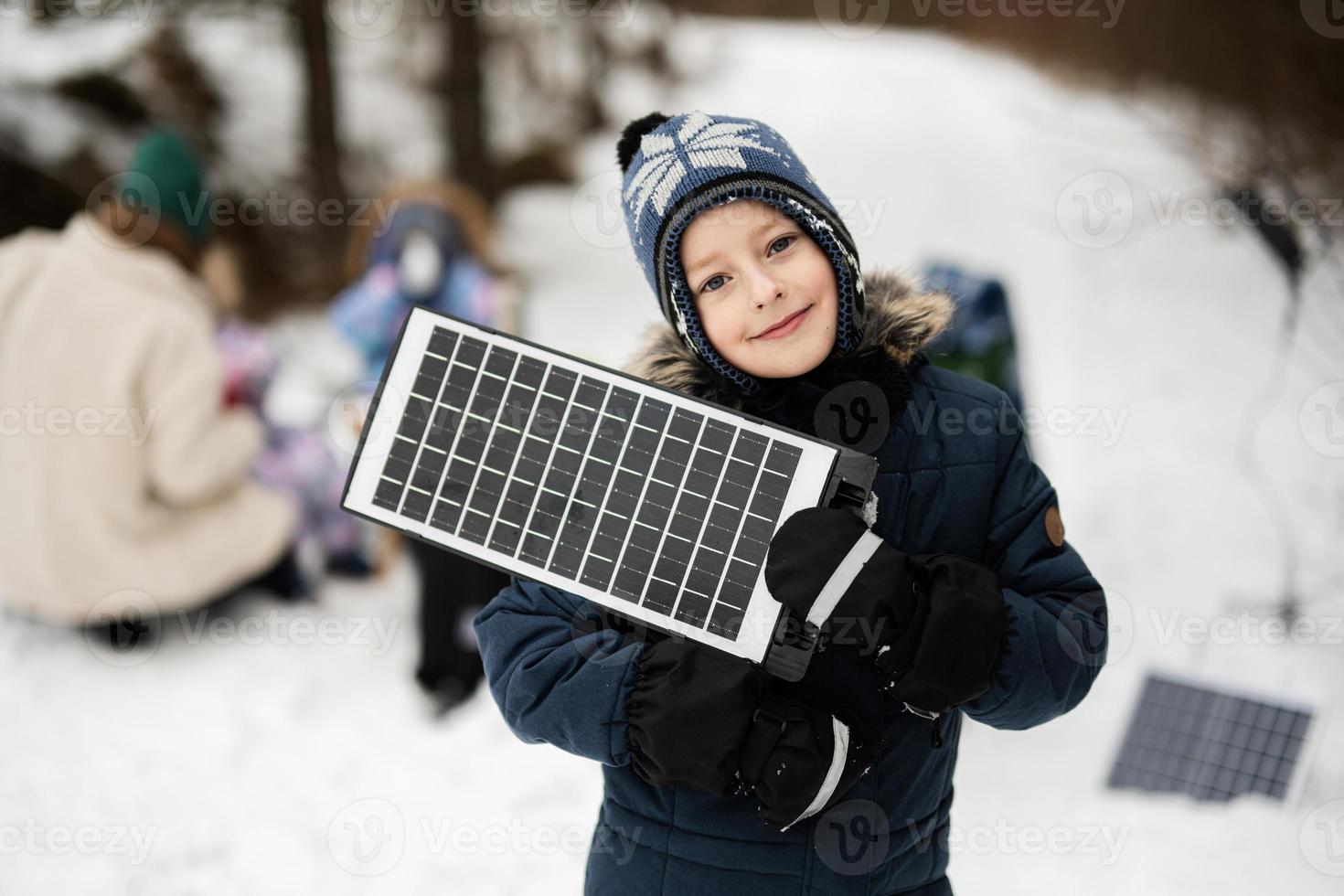 Boy with solar panel battery at hand against his family in winter forest spending time together on a picnic. photo