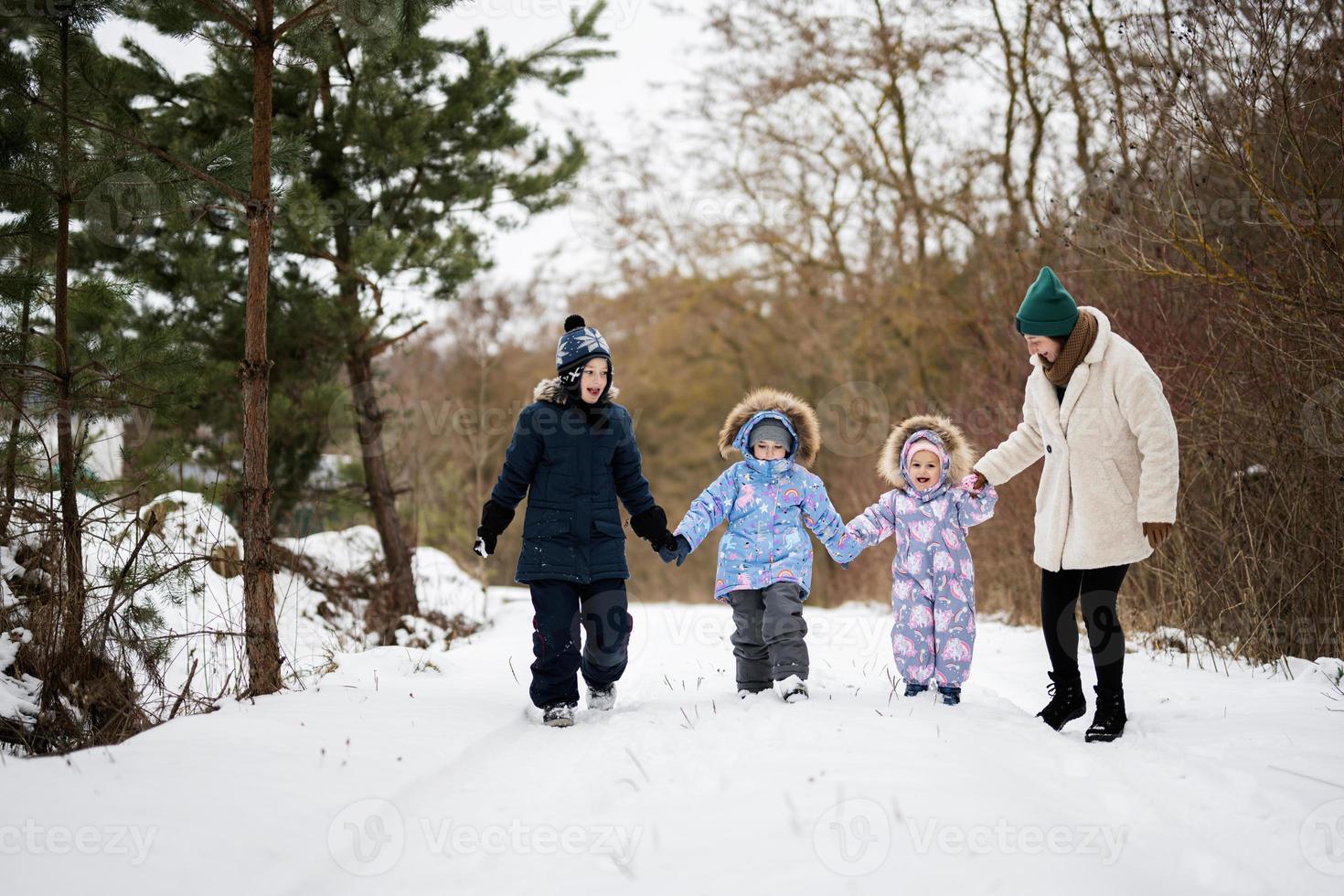 Mother with three kids holding hands and walking in winter forest. photo