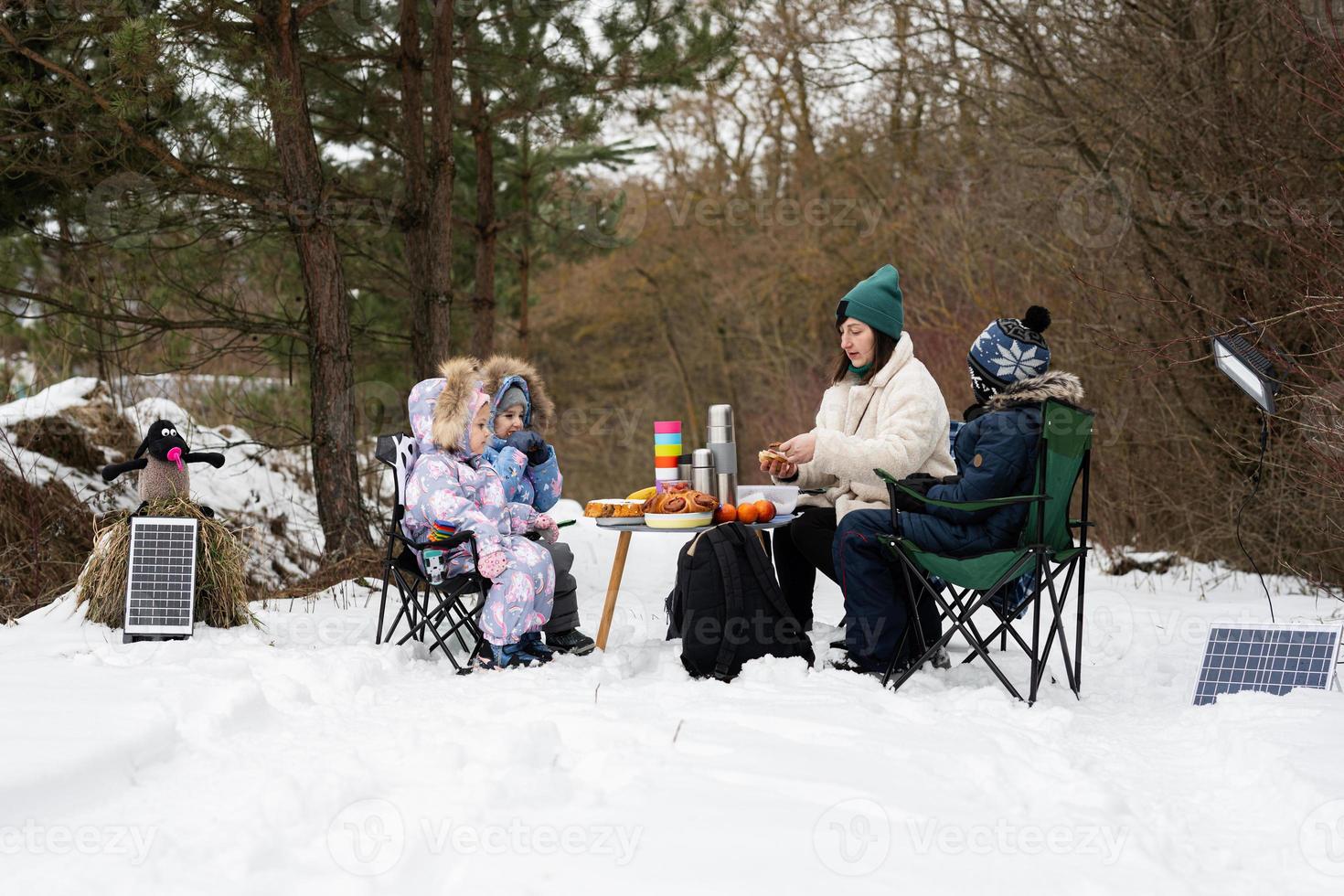 Young woman with children in winter forest on a picnic. Mother and three kids. photo