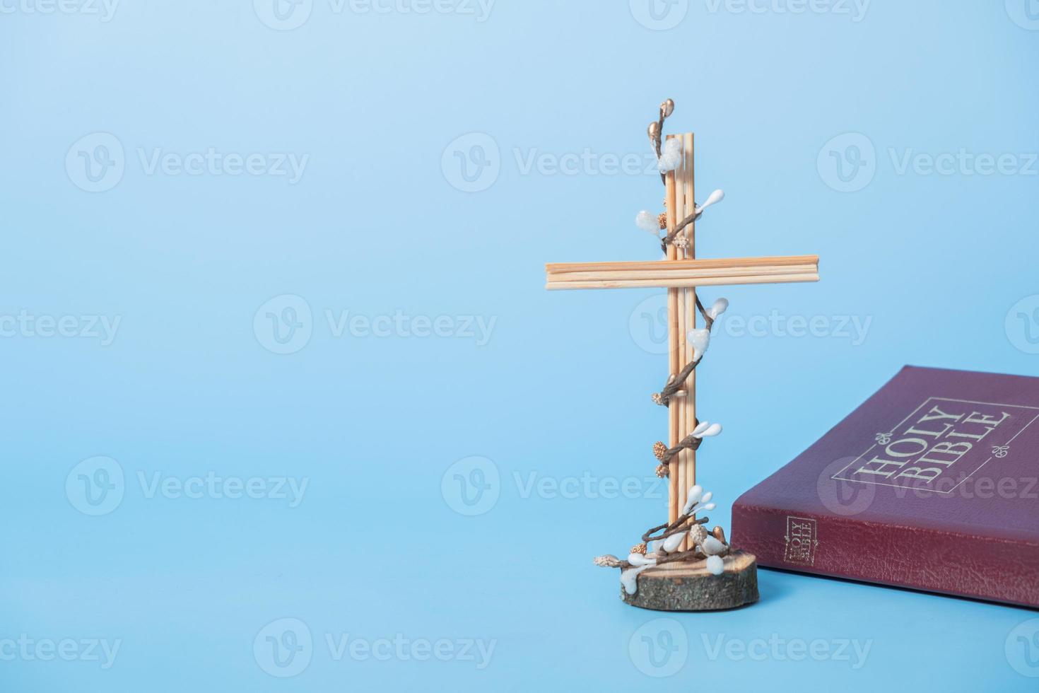 Cross decorated flowers with Holy Bible on blue background. Easter holiday minimalistic concept. Copy space photo